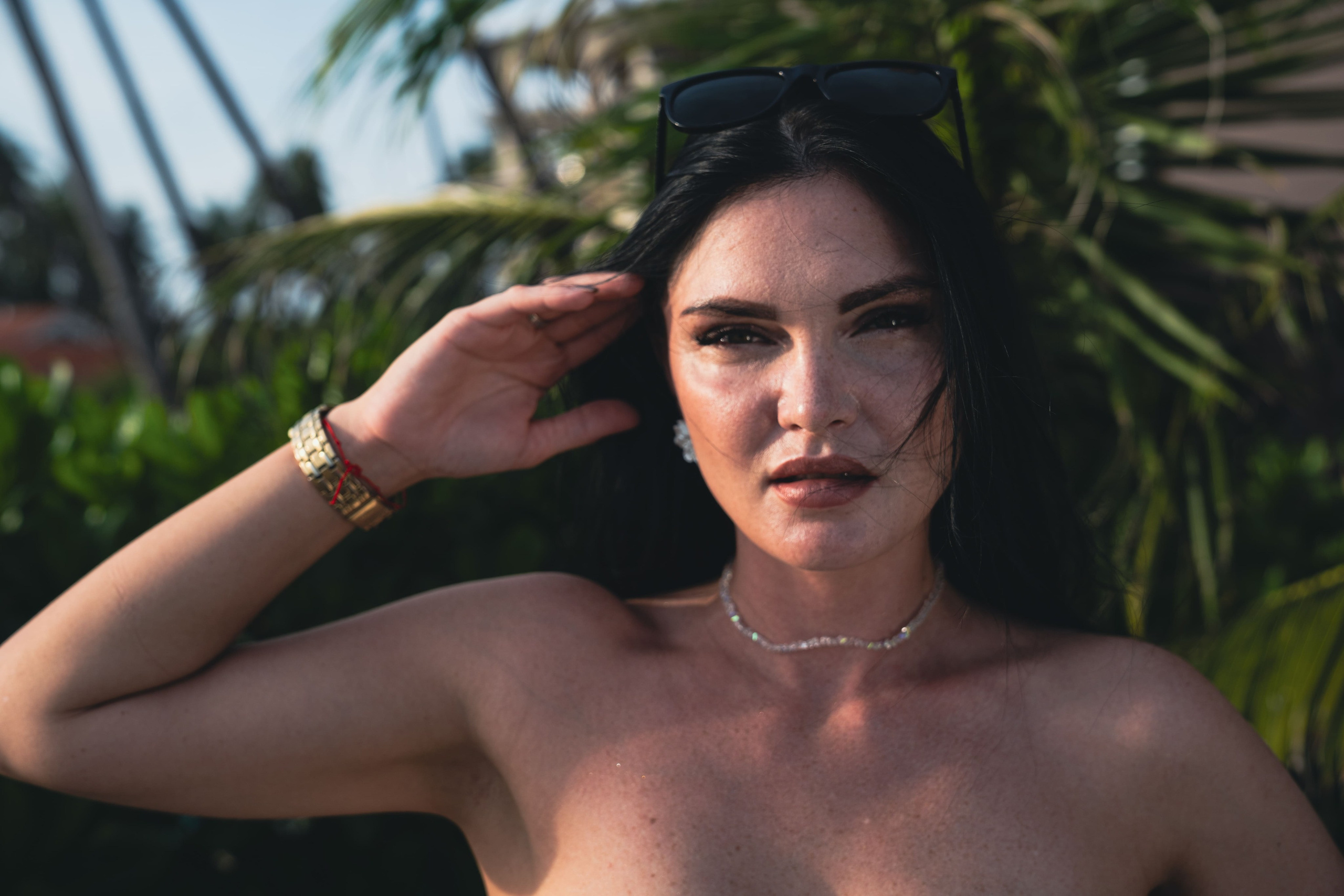 Крупный план девушки с темными волосами на фоне экзотических растений, мягкий свет.