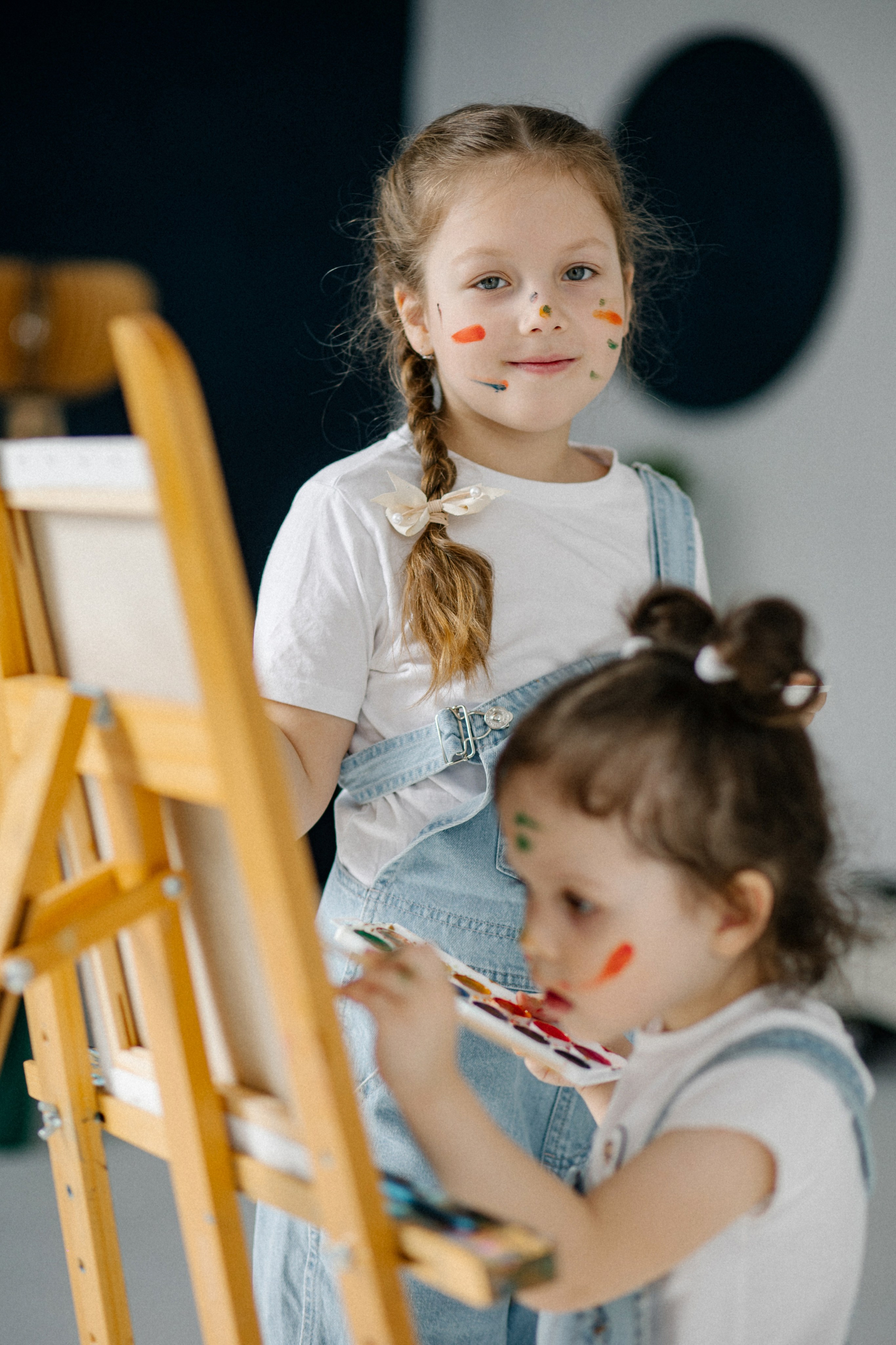 Семейная фотосъёмка в студии: две сестрички с косичками рисуют красками на холсте. Дурачество и смех в кадре от фотографа Клещинова Алексея