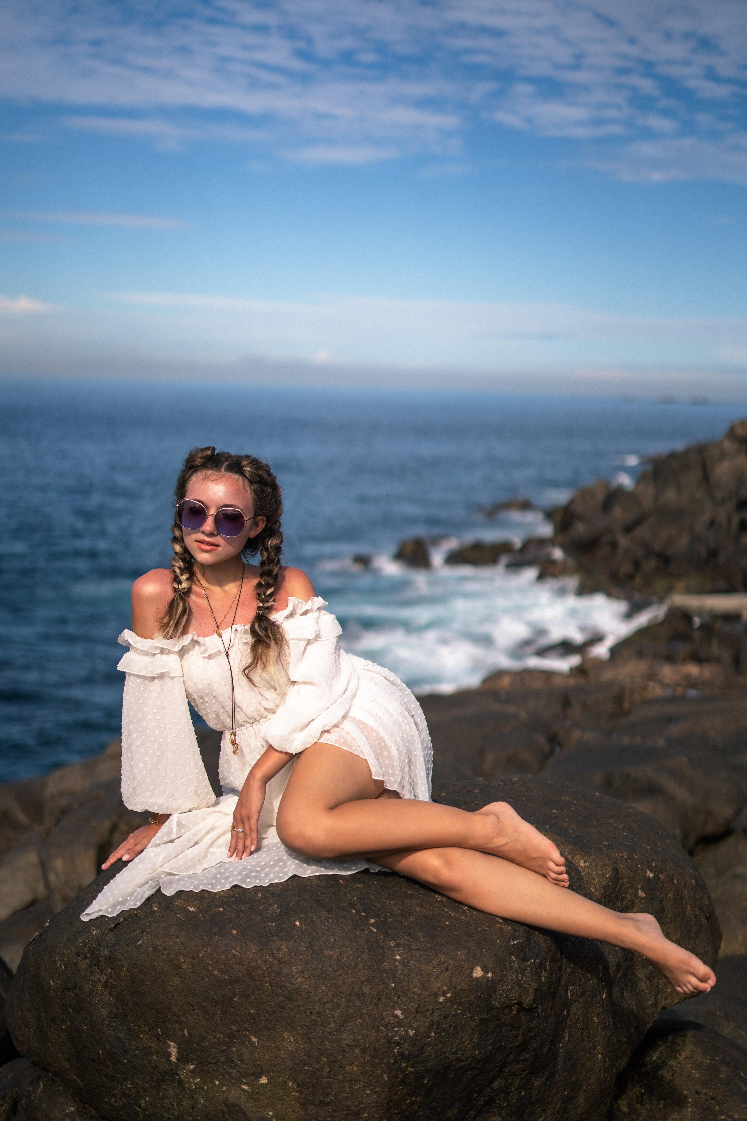 a young beauty in a white dress and glasses with the wind in her hair on the rocks