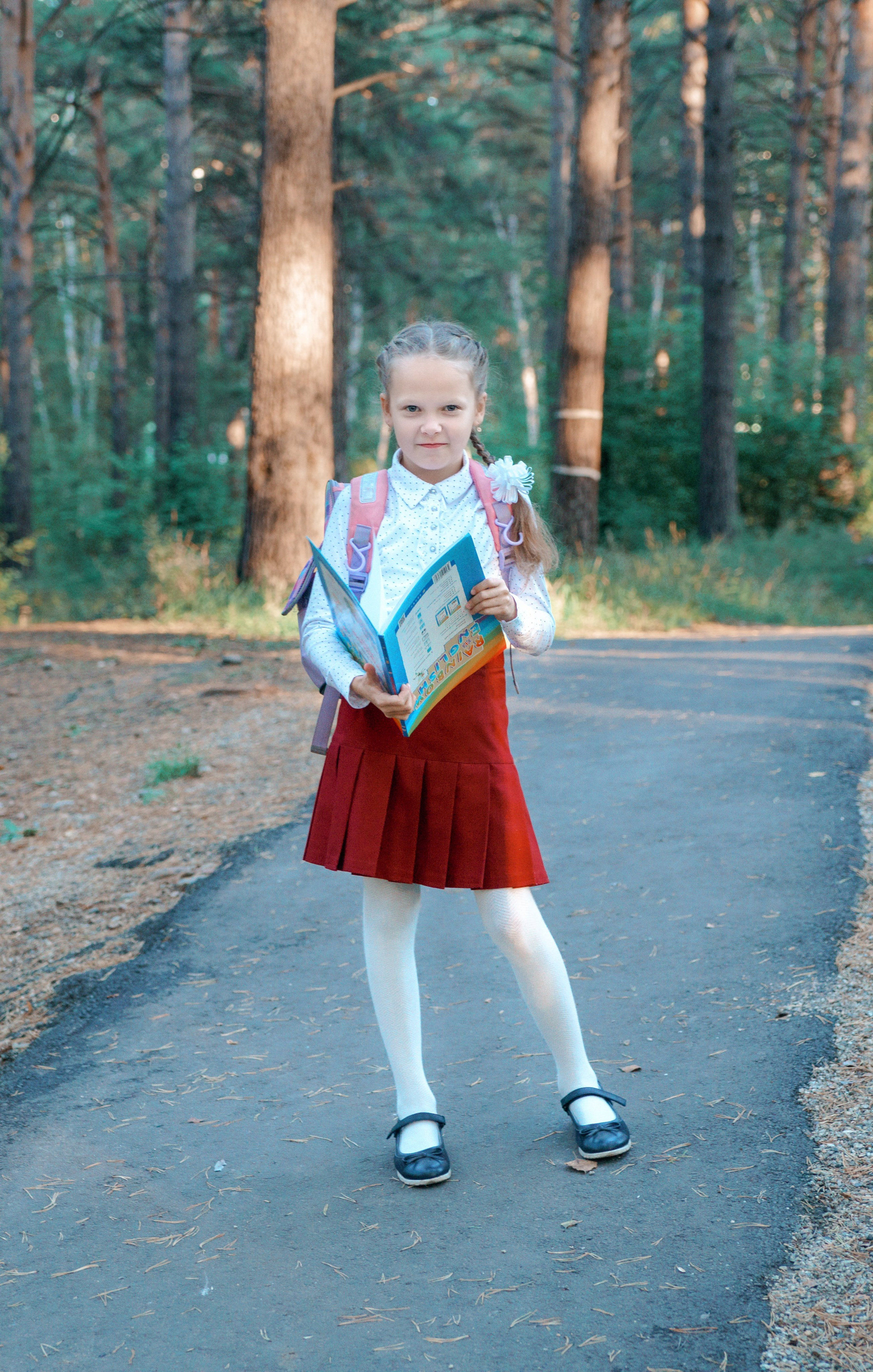 Детская фотосессия осенью - школьница стоя с учебником в лесу