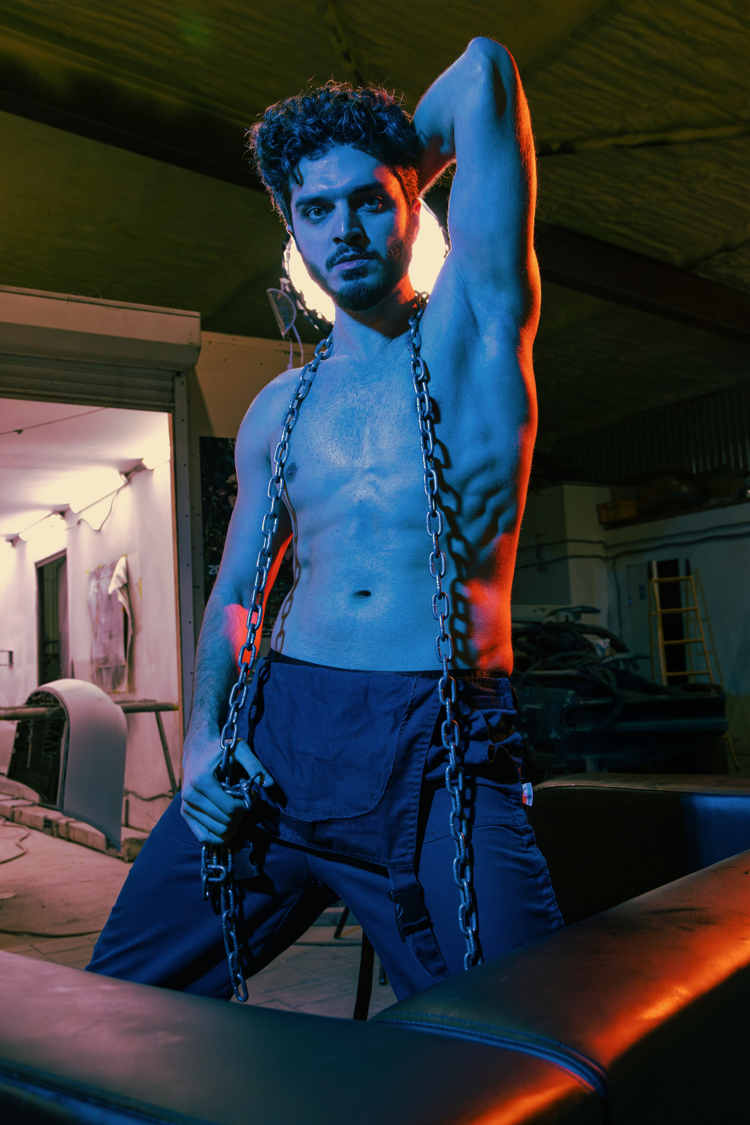 Эпатажная фотосессия в индустриальной локации, где мужское тело становится главным объектом искусства, а цветной свет усиливает драматизм композиции.