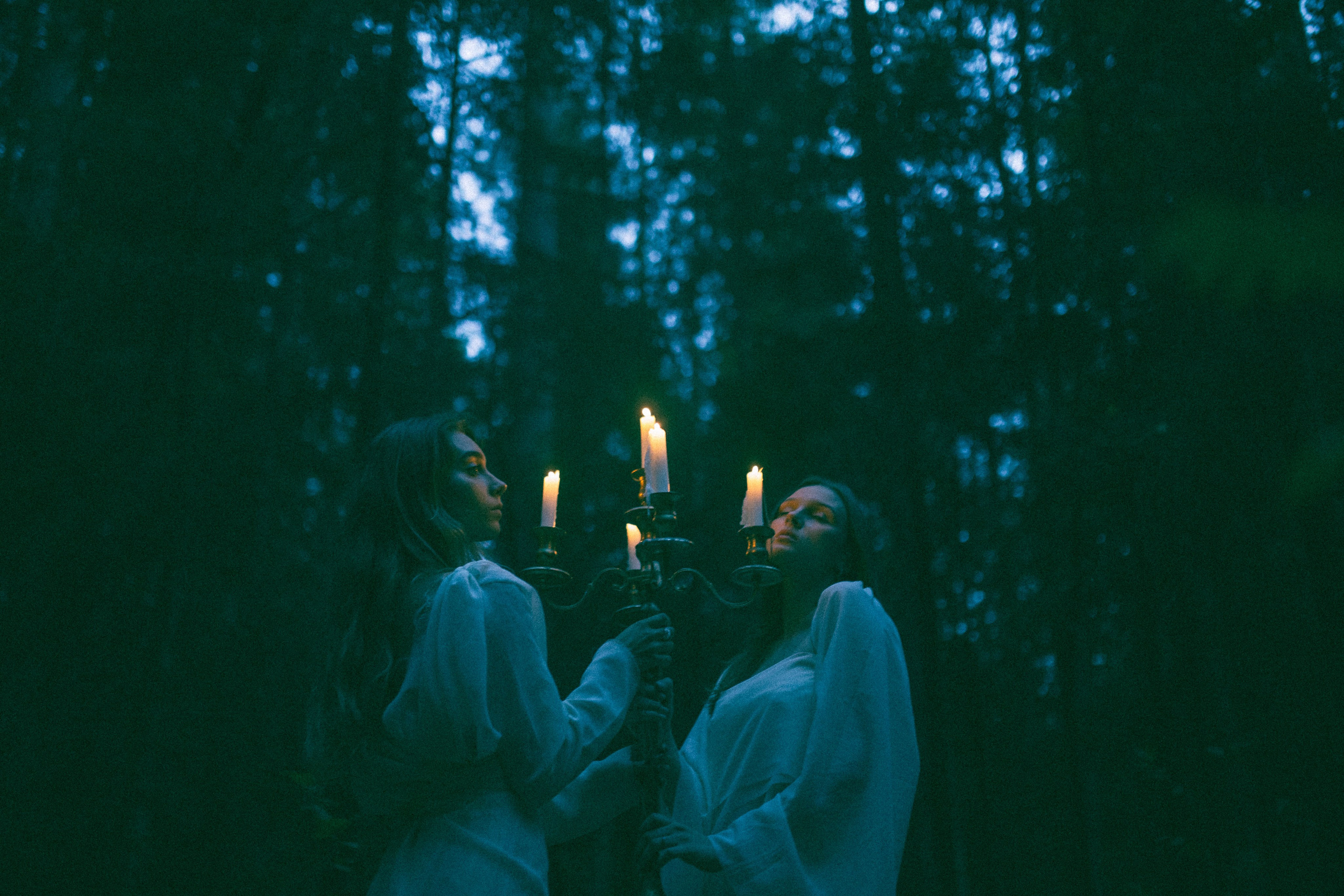 Две девушки в лесу держать в руках канделябр с горящими свечами