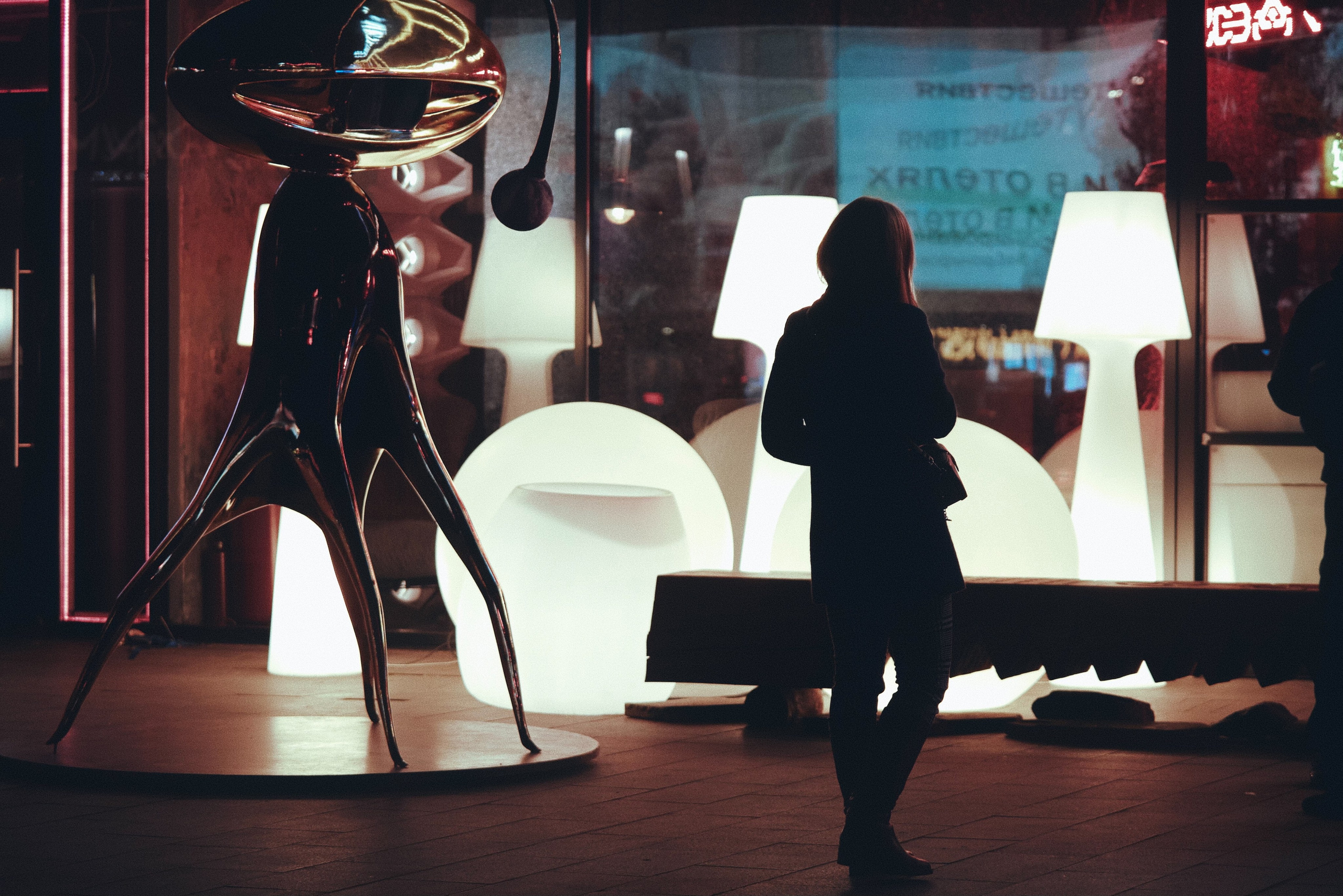 девушка подходит к светящейся витрине рядом со скульптурой на Новом Арбате