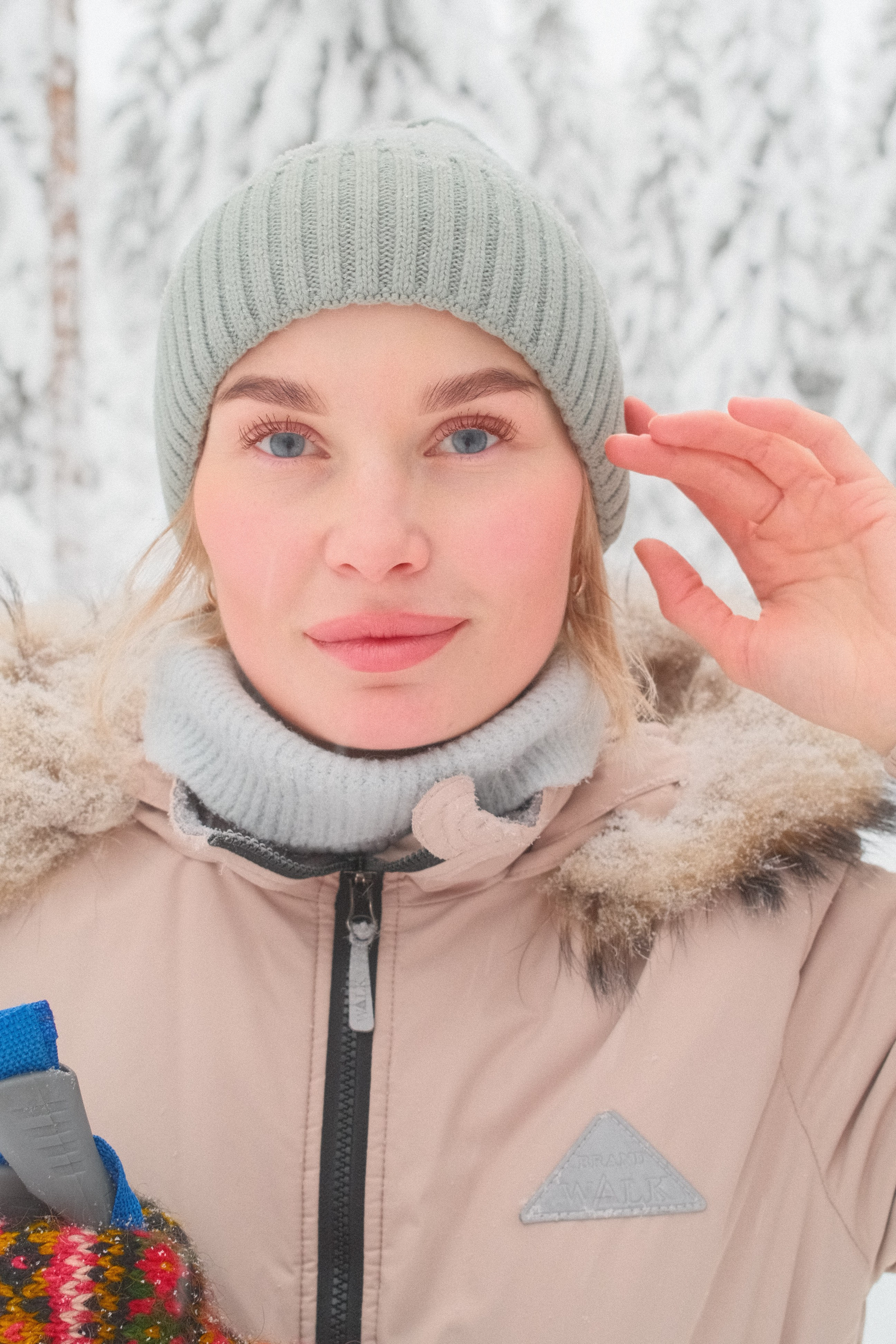 Портрет девушки с голубыми глазами в вязаной шапке в зимнем лесу