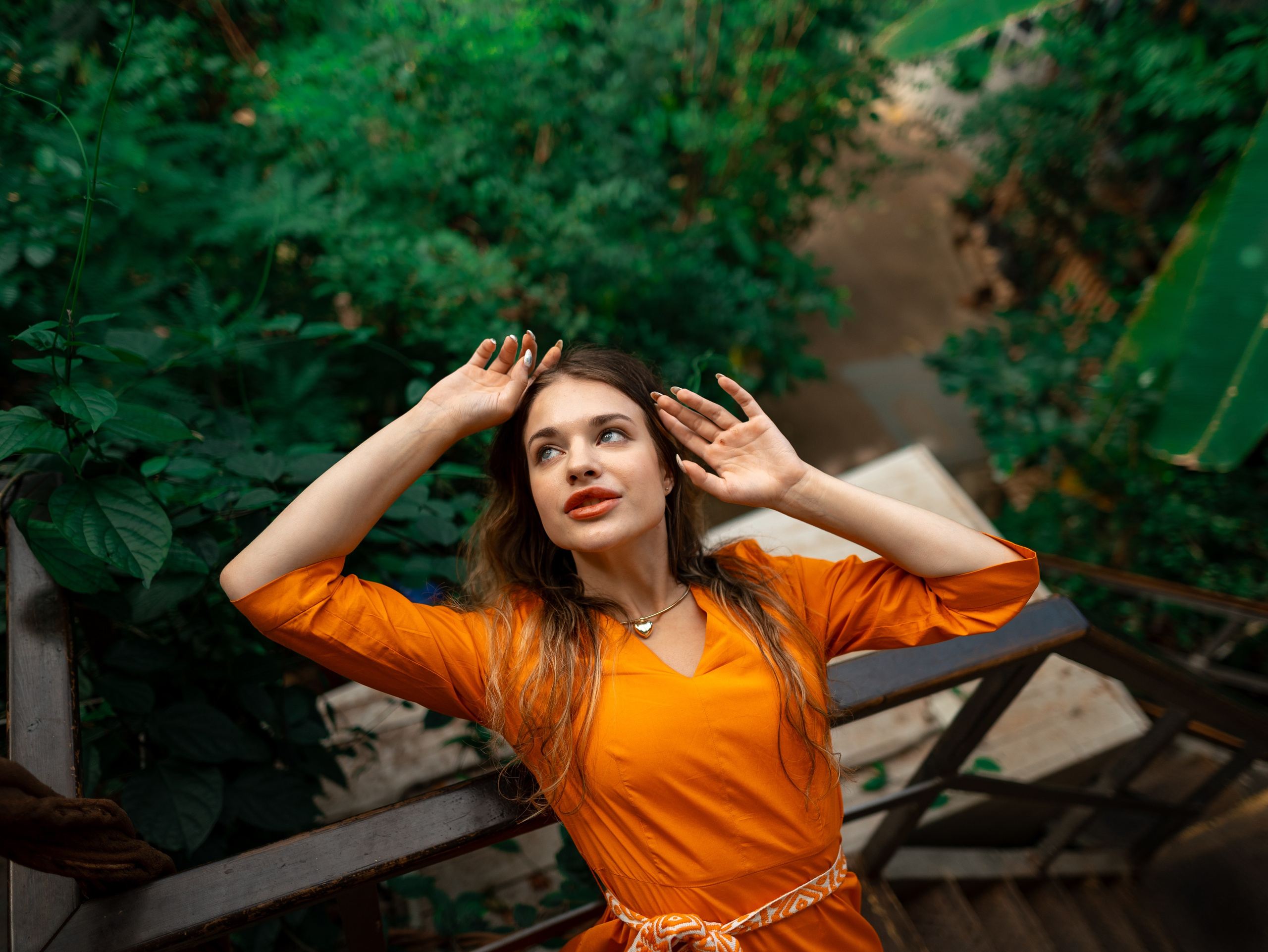 Девушка в оранжевом платье стоит на фоне зелени