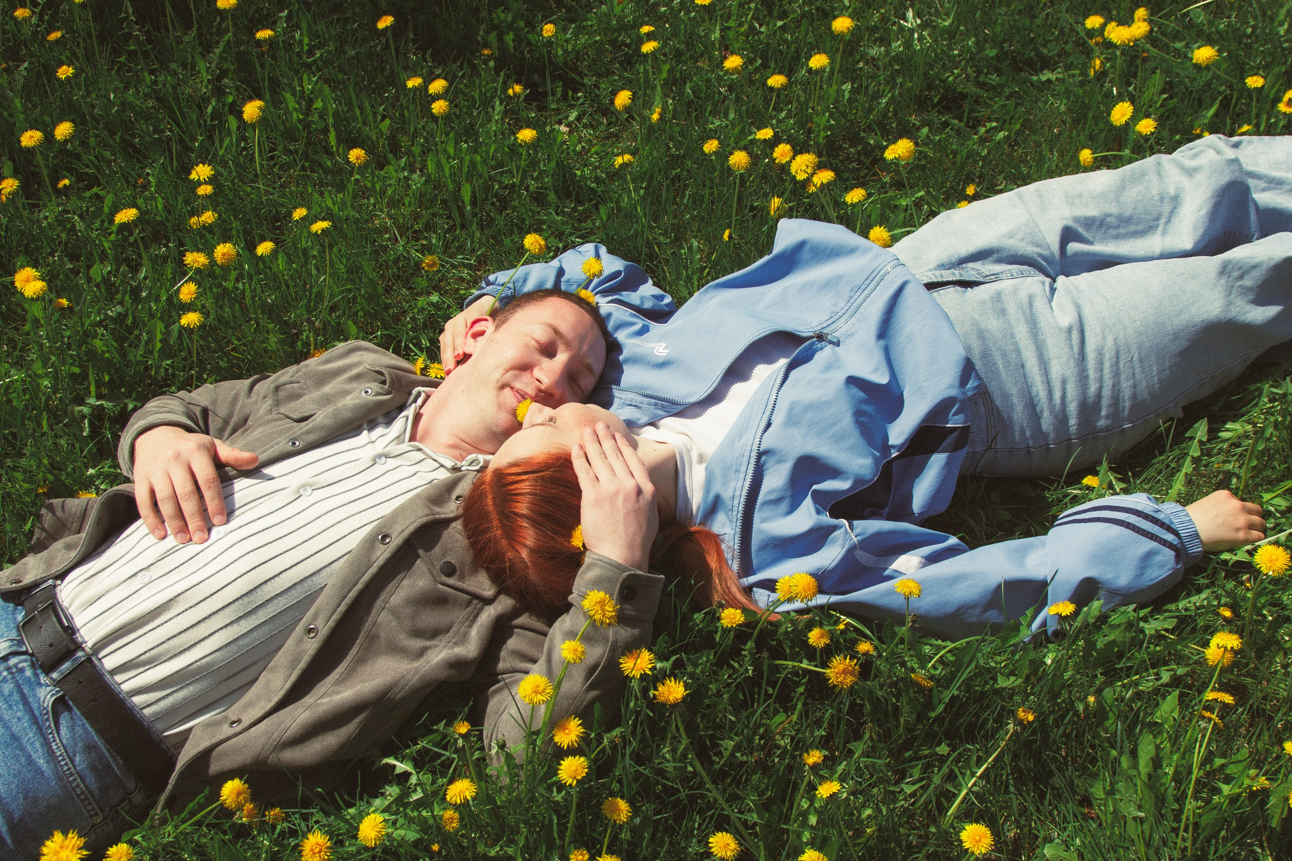 Para lezhit na trave s zholtymi tsvetami, lyubovnaya istoriya, romantichnyy portret, svadebnyy fotograf