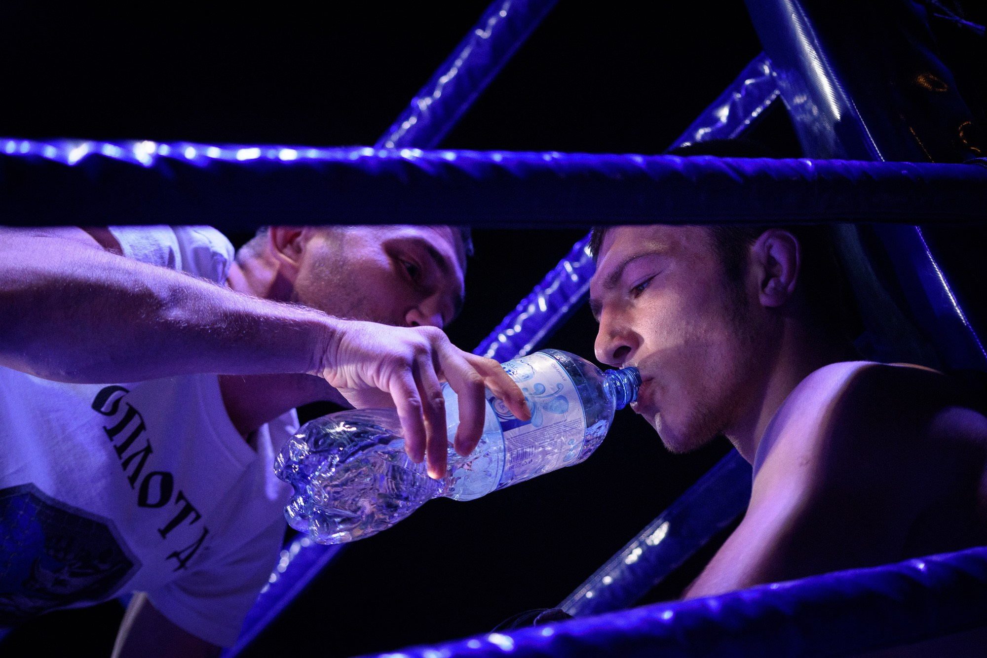 Помощник спортсмена даёт бойцу напиться из бутылки в перерыве между раундами