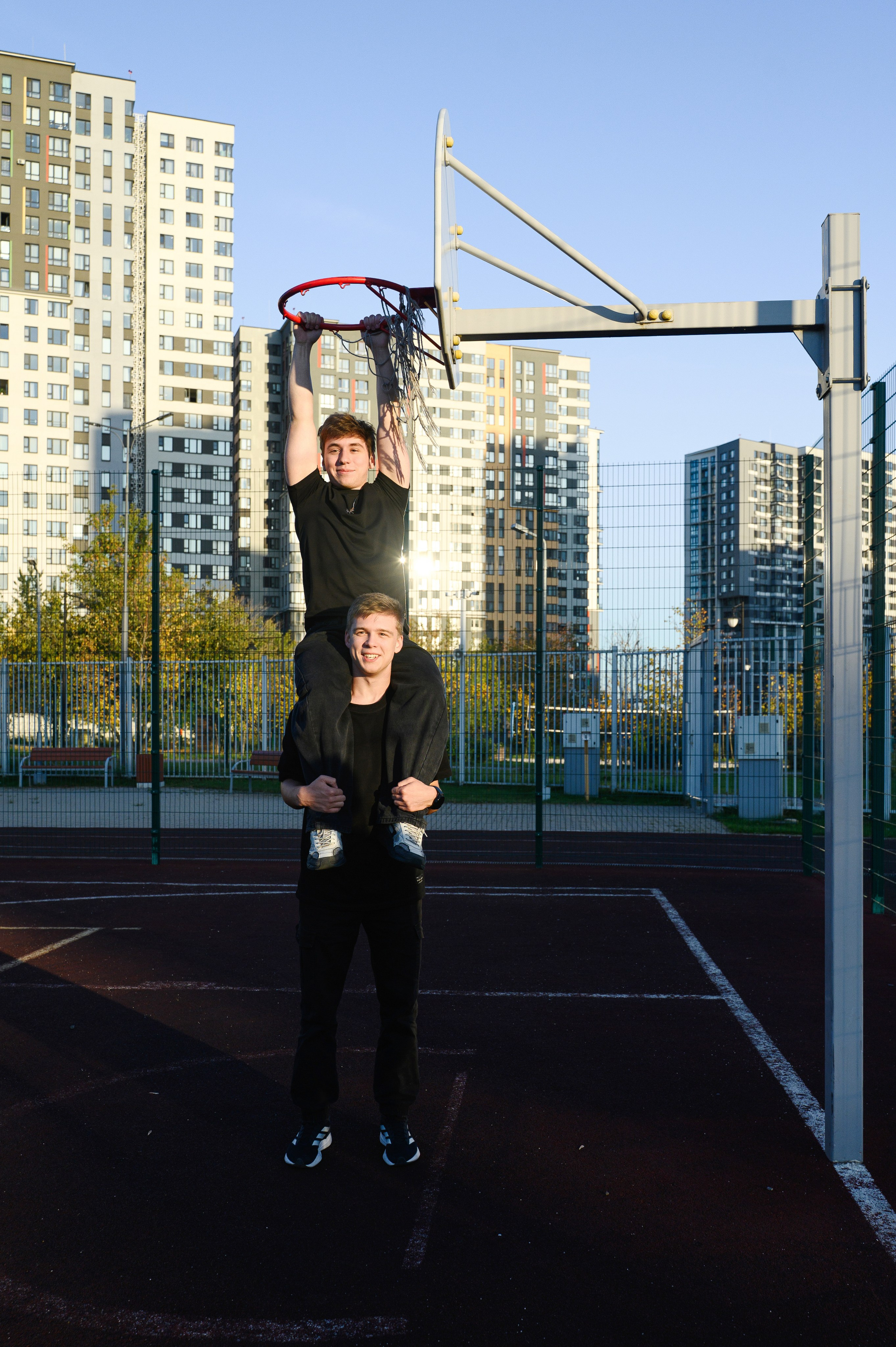 Вертикальный портрет двух выпускников у спортивной площадки на фоне жилых высоток.