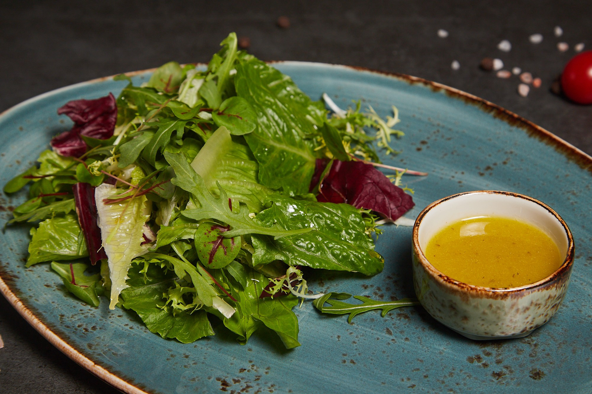Фуд-фотография салата с листьями зелени и соусом на голубой тарелке.