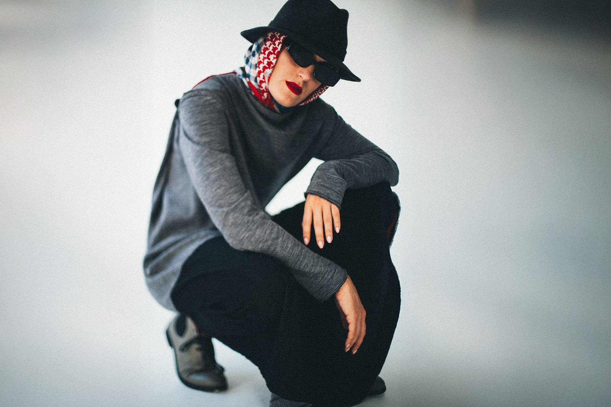Смелый fashion-кадр от фотографа Сочи Галины Скорик. Девушка в сером лонгсливе, черной шляпе и солнцезащитных очках позирует на светлом минималистичном фоне. Под шляпой виден яркий платок, добавляющий образу графичности.