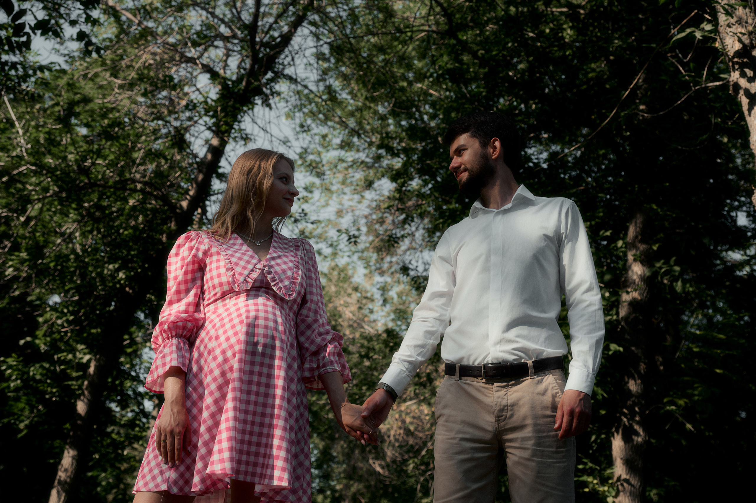 Елизавета и Юрий держатся за руки, стоя под деревьями.