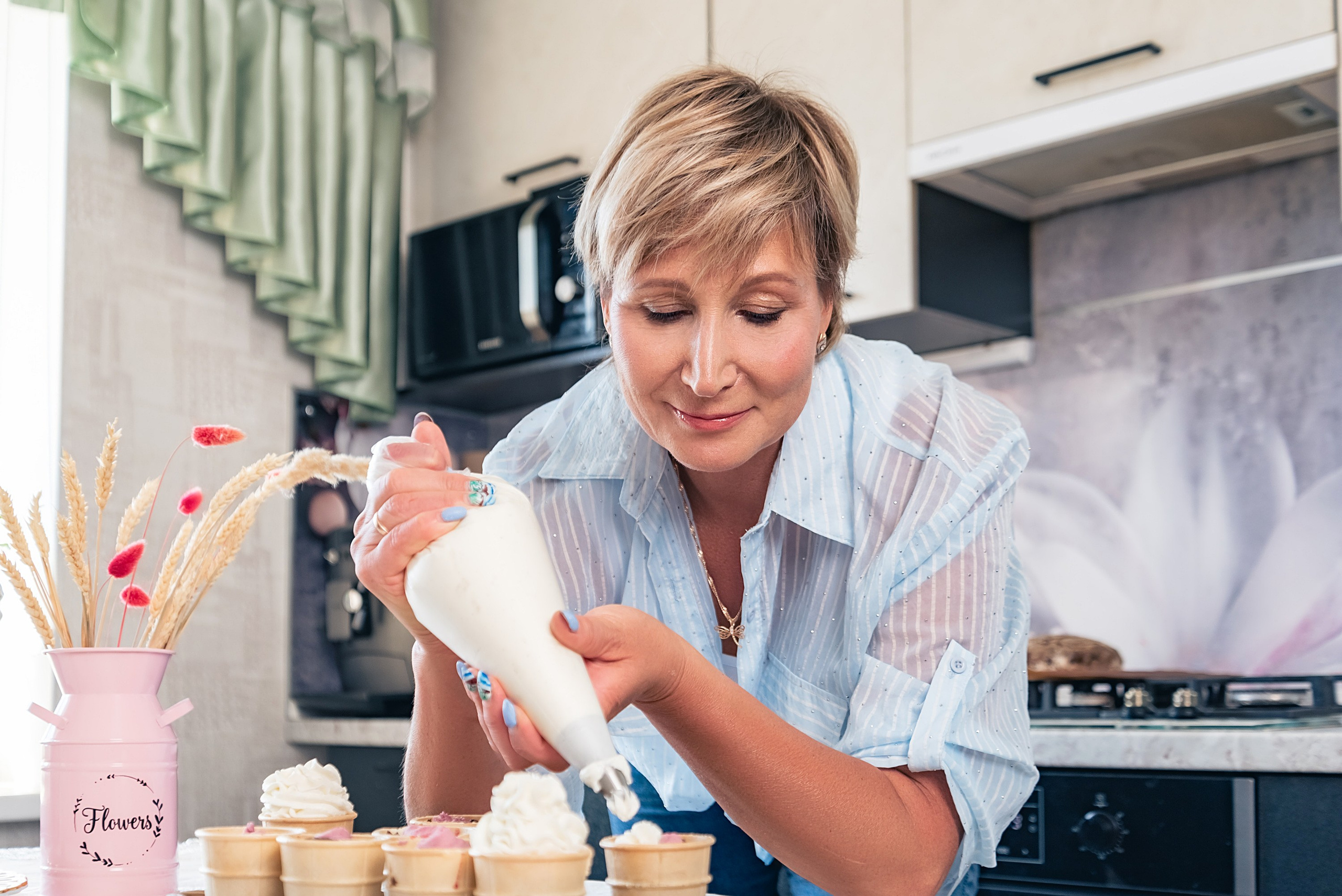 На фото женщина на кухне украшает выпечку.