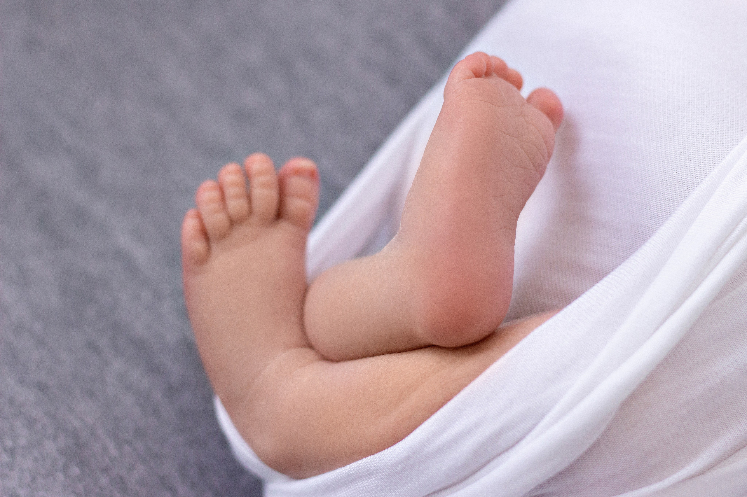 краснодар, высунутые ножки новорожденного с коликами беспокойным животиком в бело-серых тонах, после успокоения, укатанные в обмотку