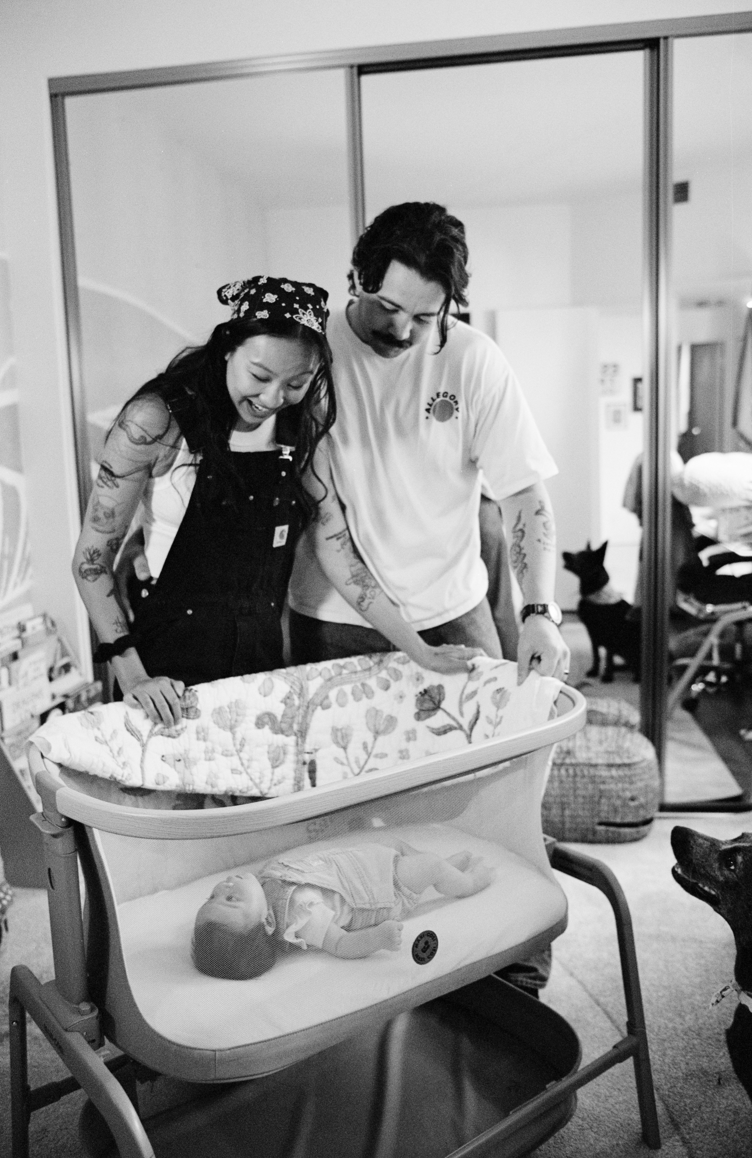 New parents overlooking the crib with the baby girl in her nursery on black and white film