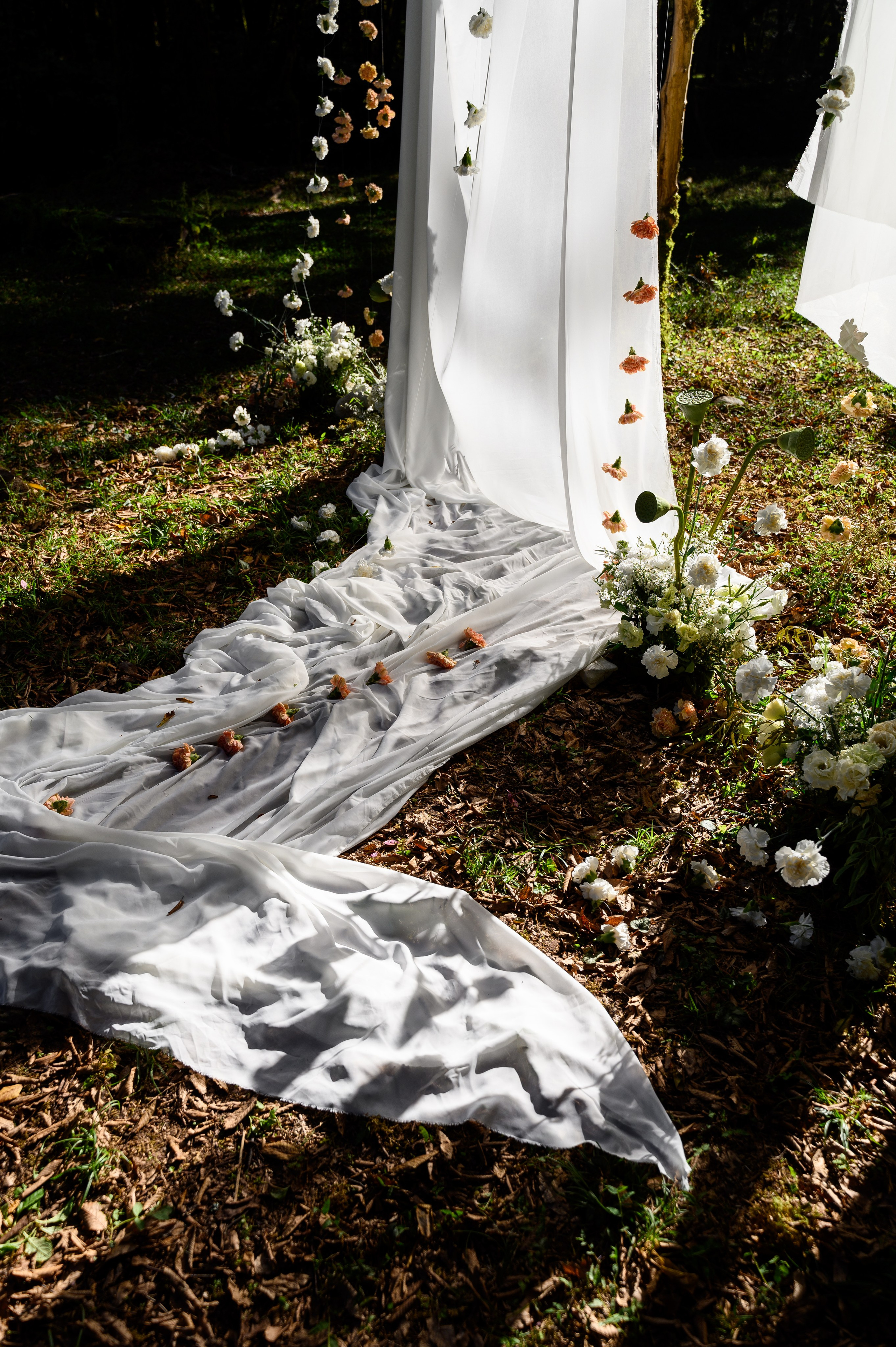 Белая ткань разложенная на земле на которой разбросаны цветы все это часть свадебного декора 