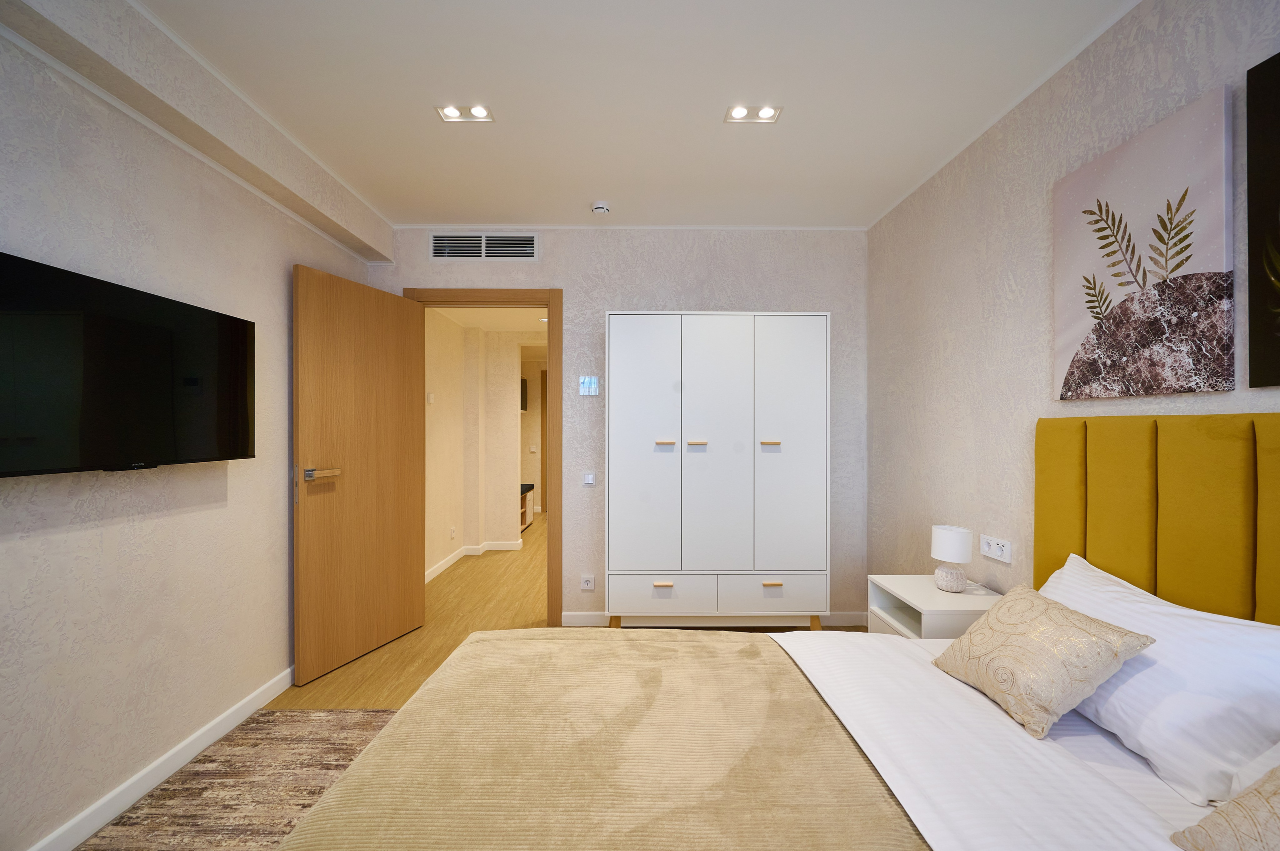 комната светлые оттенки кровать желтого цвета белый шкаф светлые шторы телевизор белые тумбы у кровати