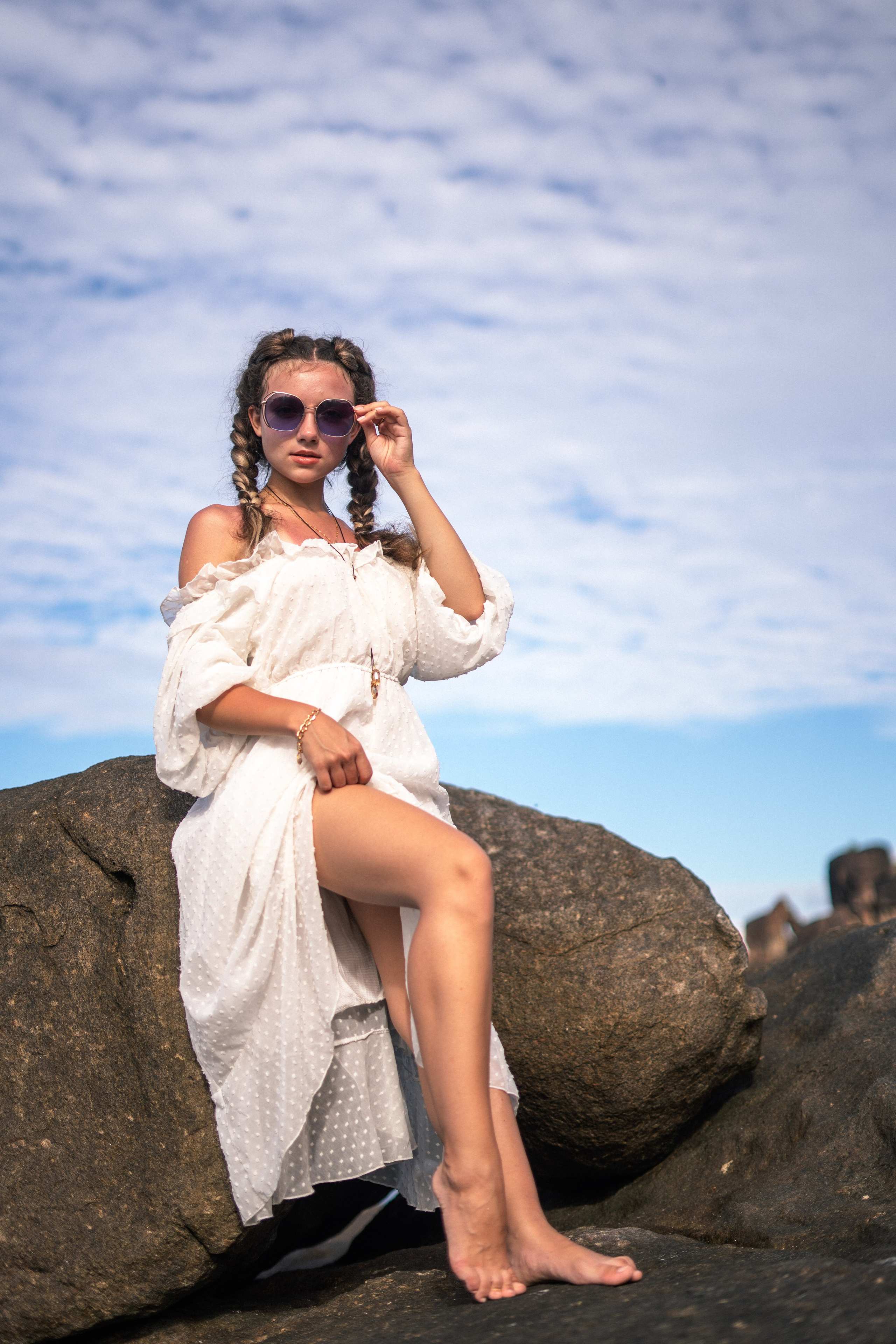a girl in a white dress and glasses enjoying a sunny day on the rocks by the ocean