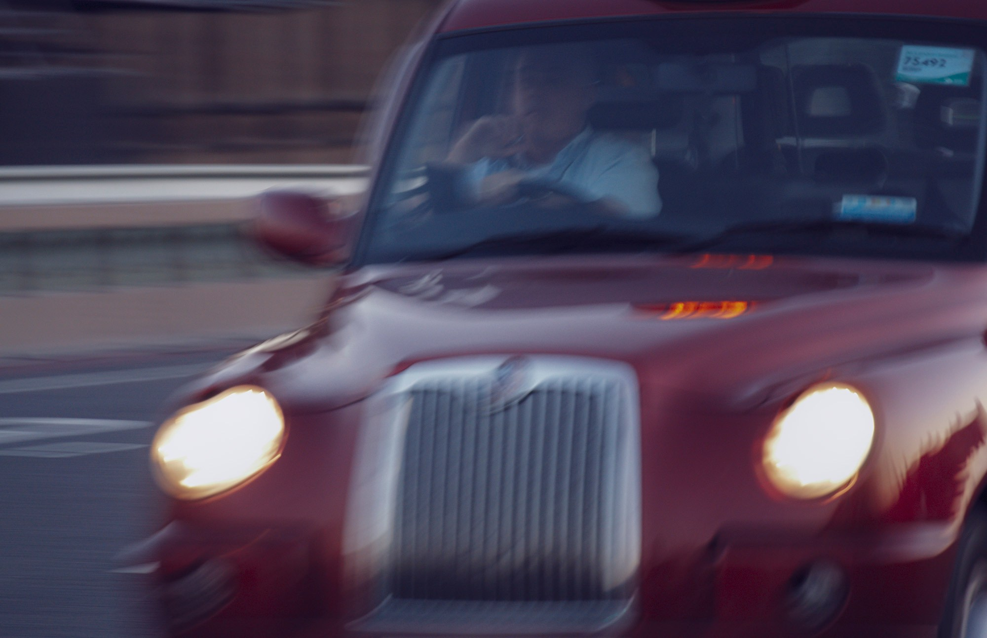 Динамичное фото красного лондонского такси в движении, эффект проводки, резкий фокус на решетке радиатора и включенных фарах, вечерний снимок