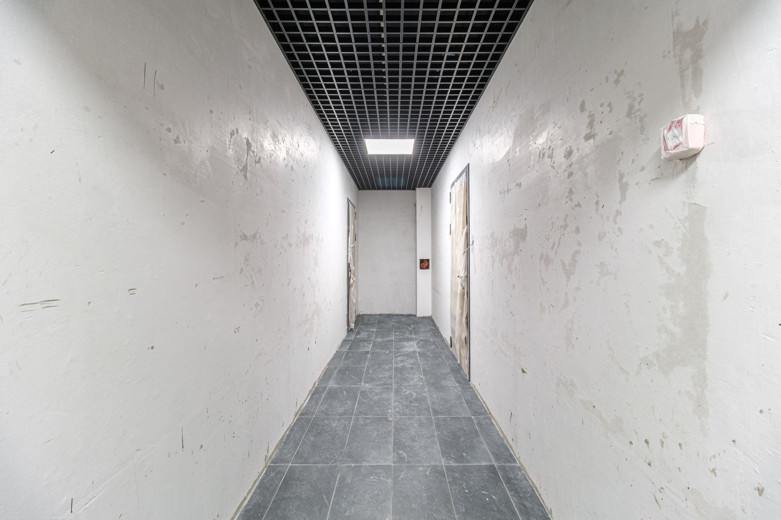 Коридор жилого комплекса. По бокам комнаты расположены двери. Пол покрыт плиткой серого цвета.