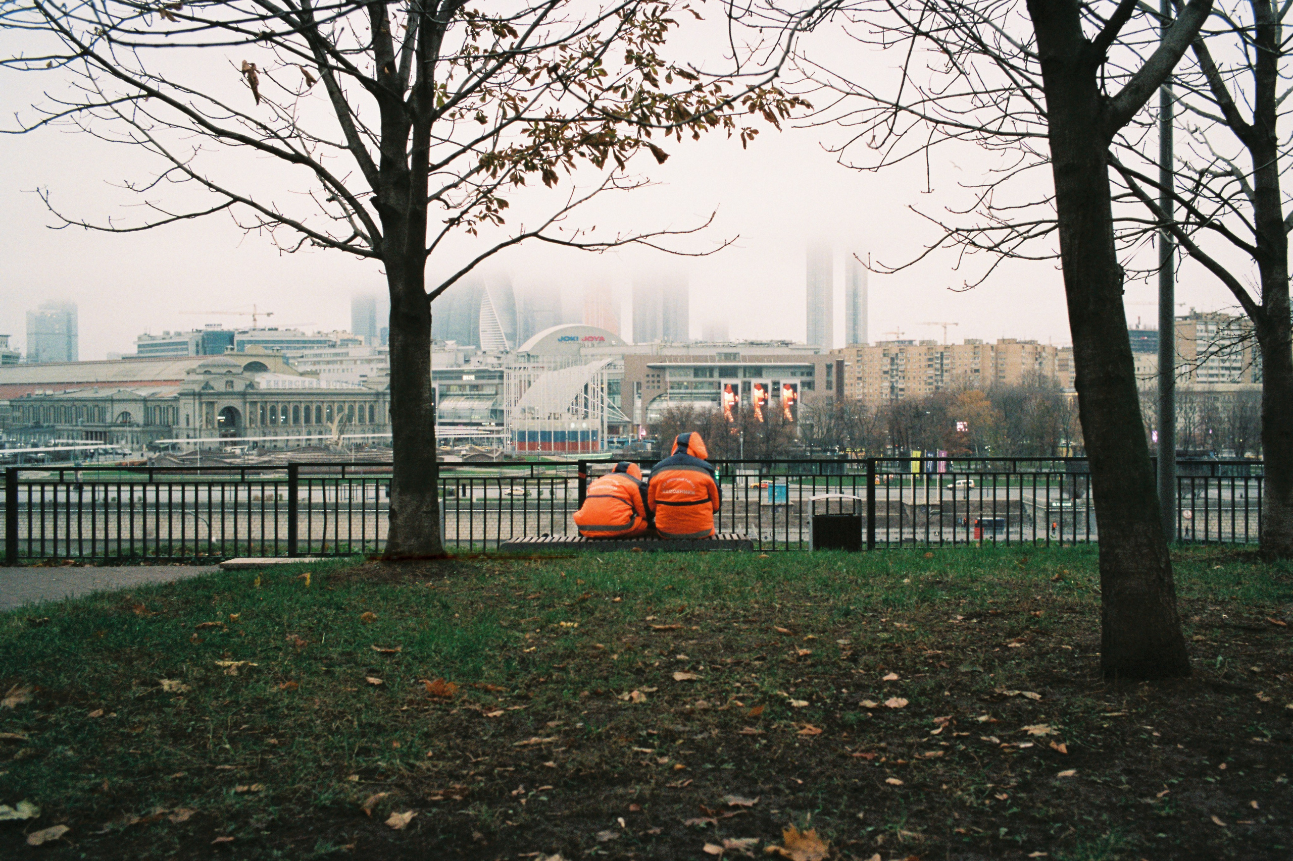Двое рабочих в оранжевых костюмах сидят на лавочке на Ростовской набережной с видом на Москва-Сити