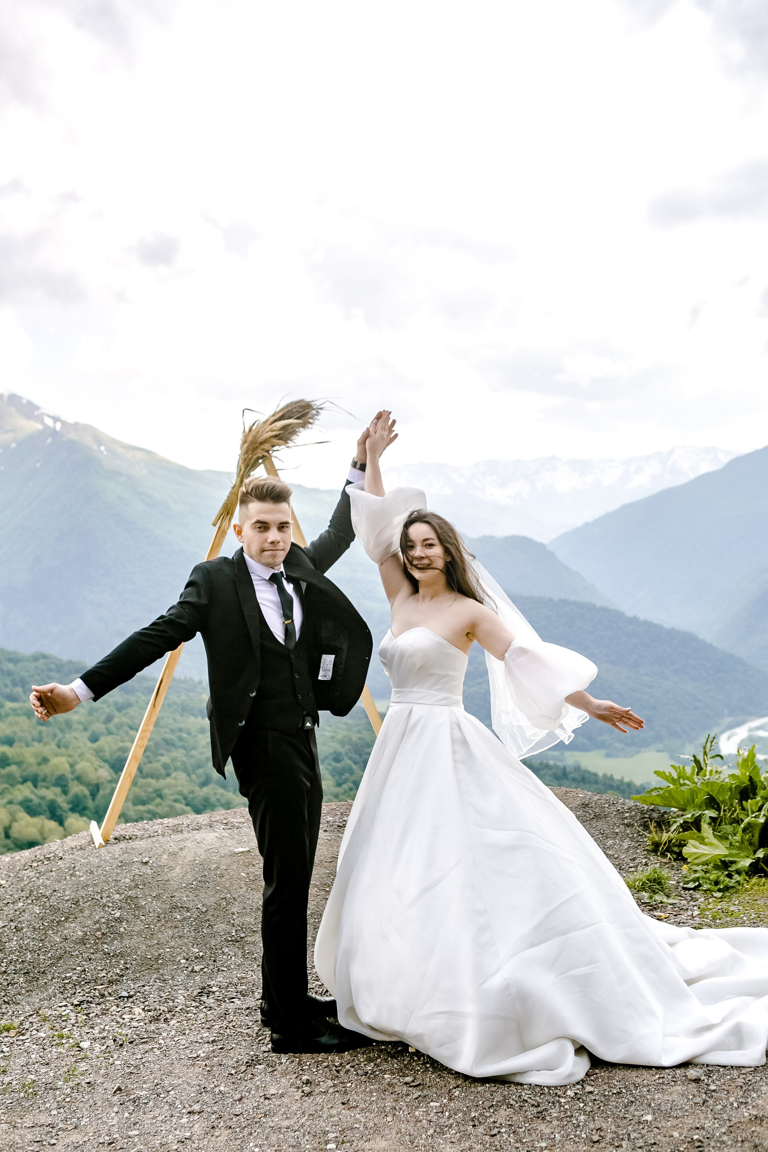 Свадебная пара на фоне величественных Кавказских гор, обнимаясь и улыбаясь друг другу