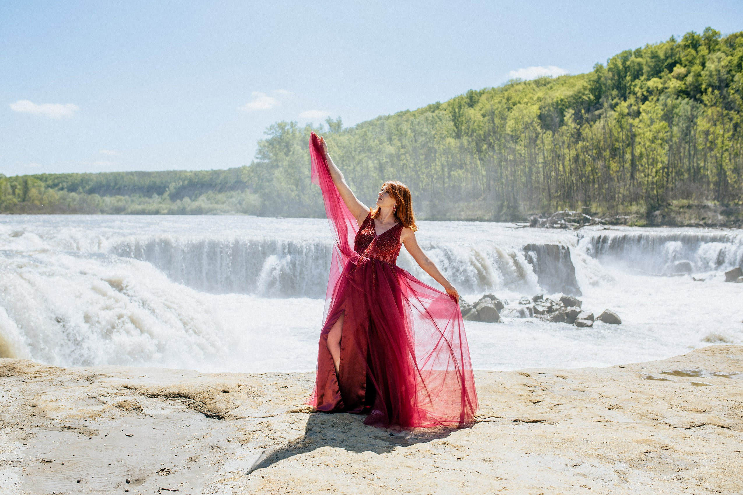 Беременная девушка в шикарном платье на фоне водопада.