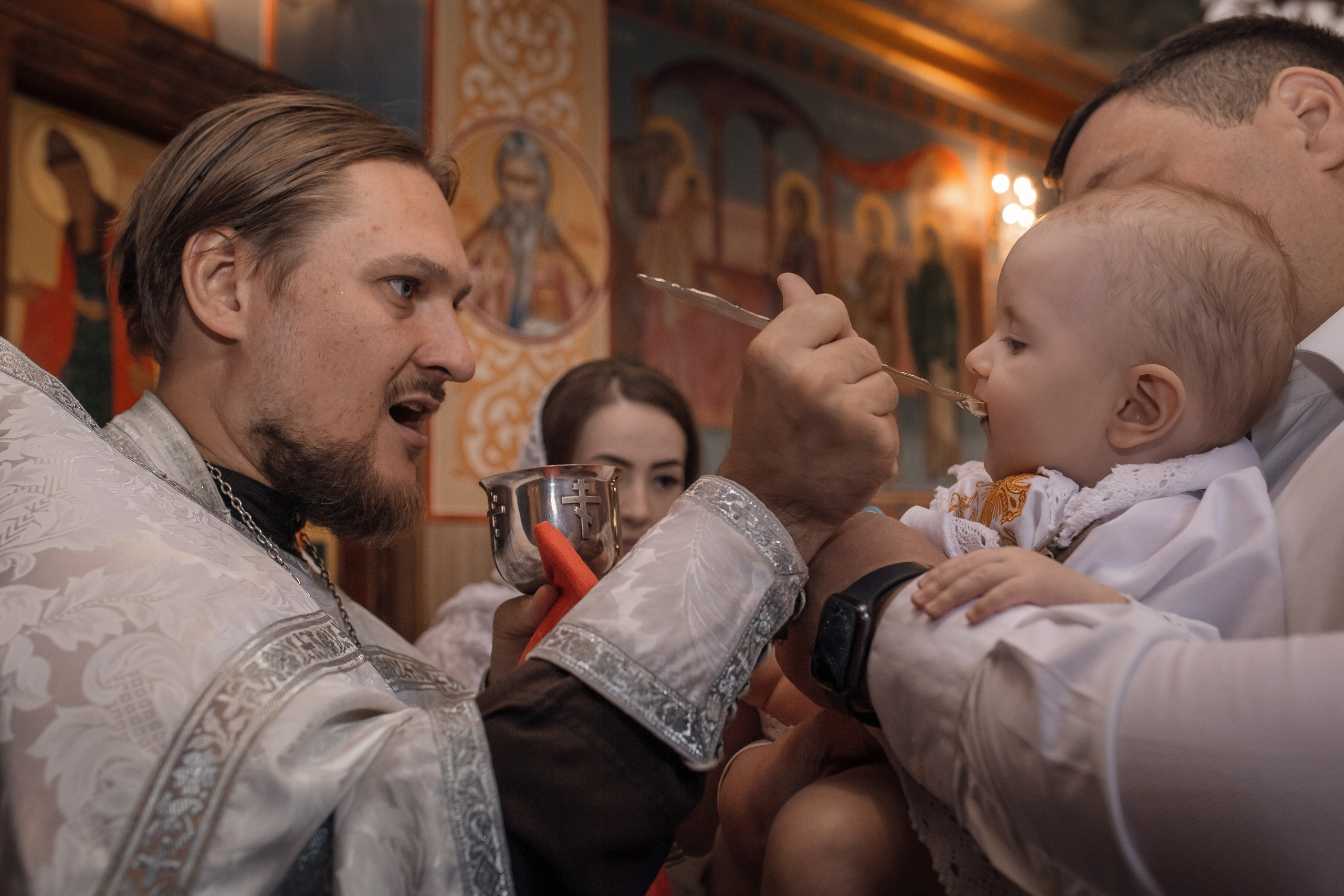 священник совершает помазание ребенка во время крестин в Ташкенте
