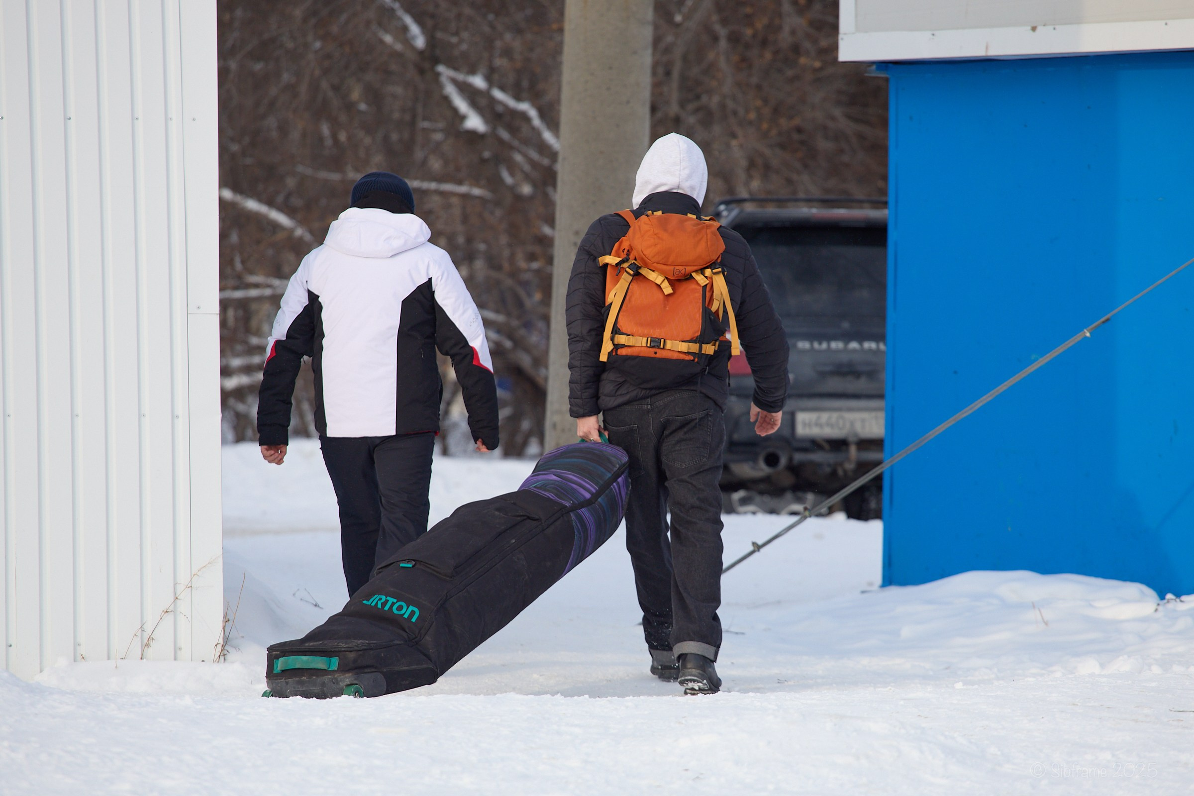 Два человека из группы поддержки участника соревнований по сноуборду уносят чехол со снаряжением