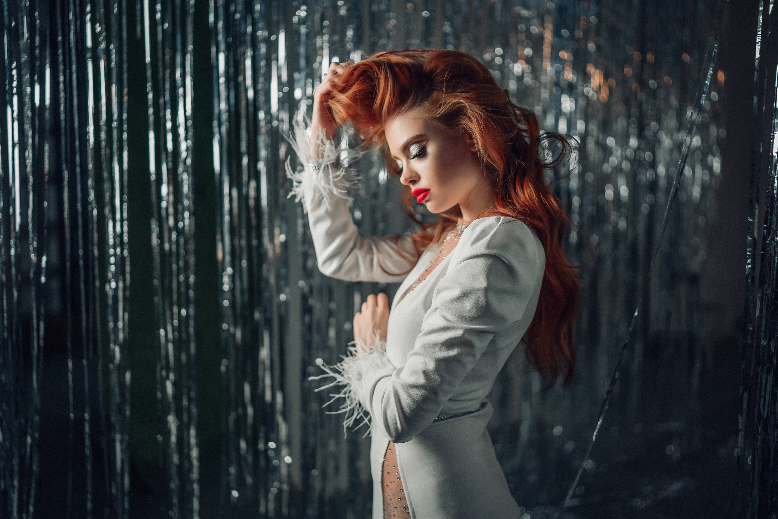 Девушка с рыжими волосами в белом платье в студии с новогодней мишурой держут волосы рукой