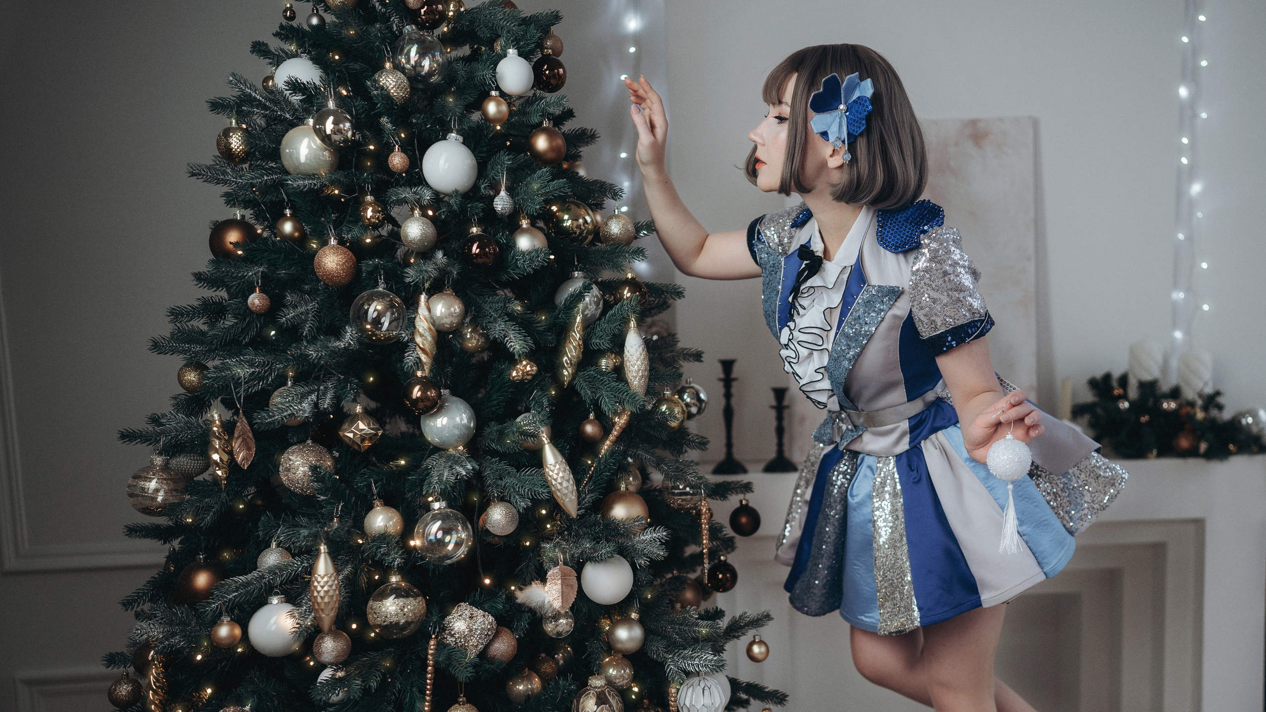 Девушка в синем платье вешает игрушки на елку.