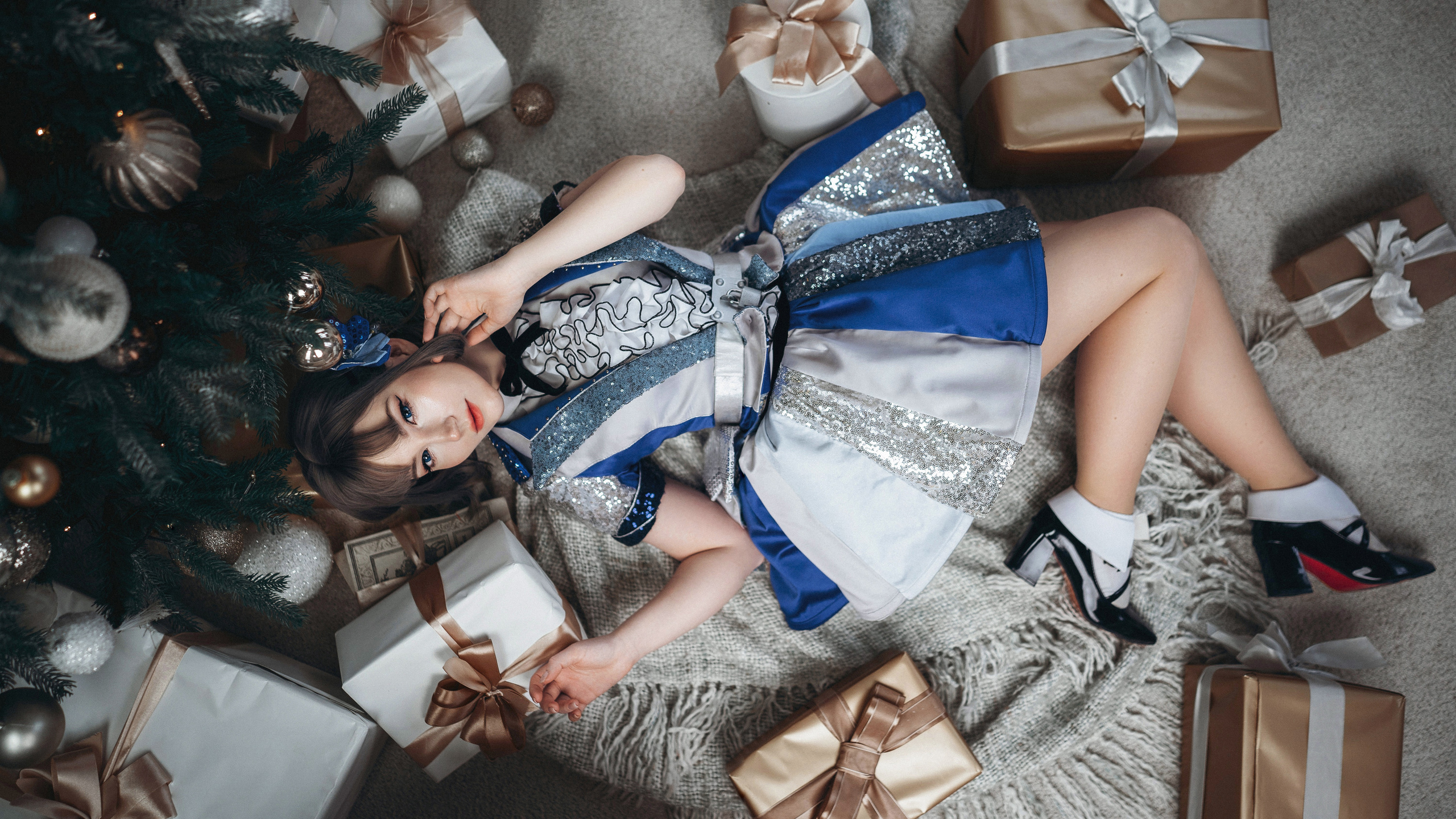 Девушка в синем платье лежит на полу у елки.