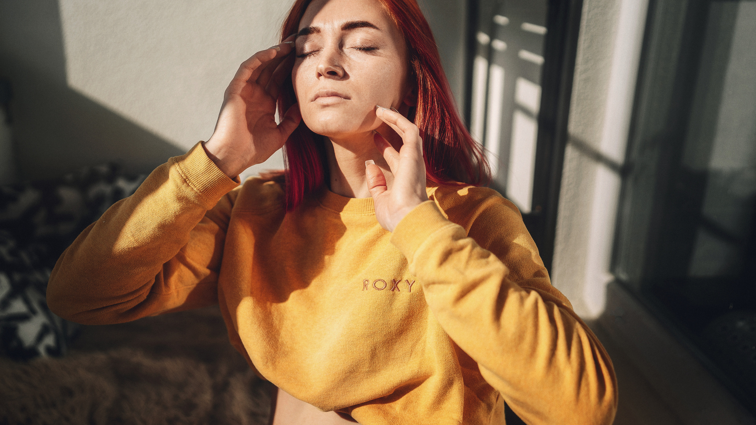 Рыженькая девушка в черных трусиках держит руки у лица, когда греет солнышко.