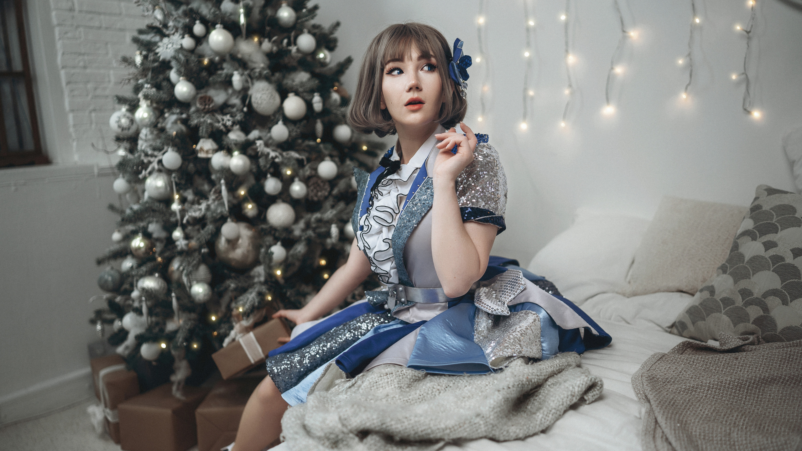 Девушка в синем платье сидит на кровати, а новогодняя елка.