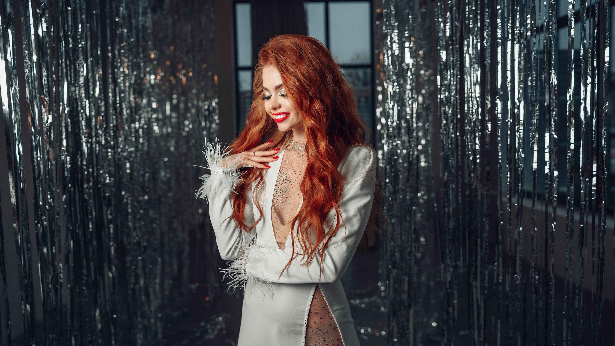 Девушка с рыжими волосами в белом платье улыбается в студии с новогодней мишурой