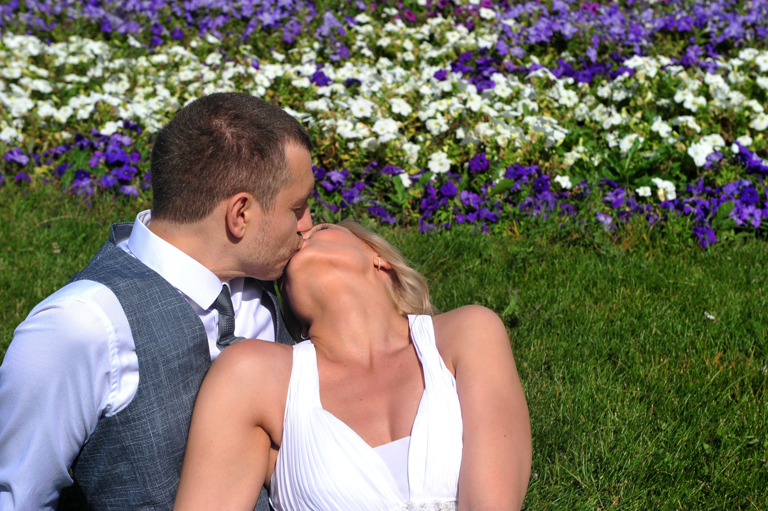 Свадьба на Воробьёвых Горах рядом с МГУ, поцелуй новобрачных на фоне зеленой лужайки и сине-белых цветов