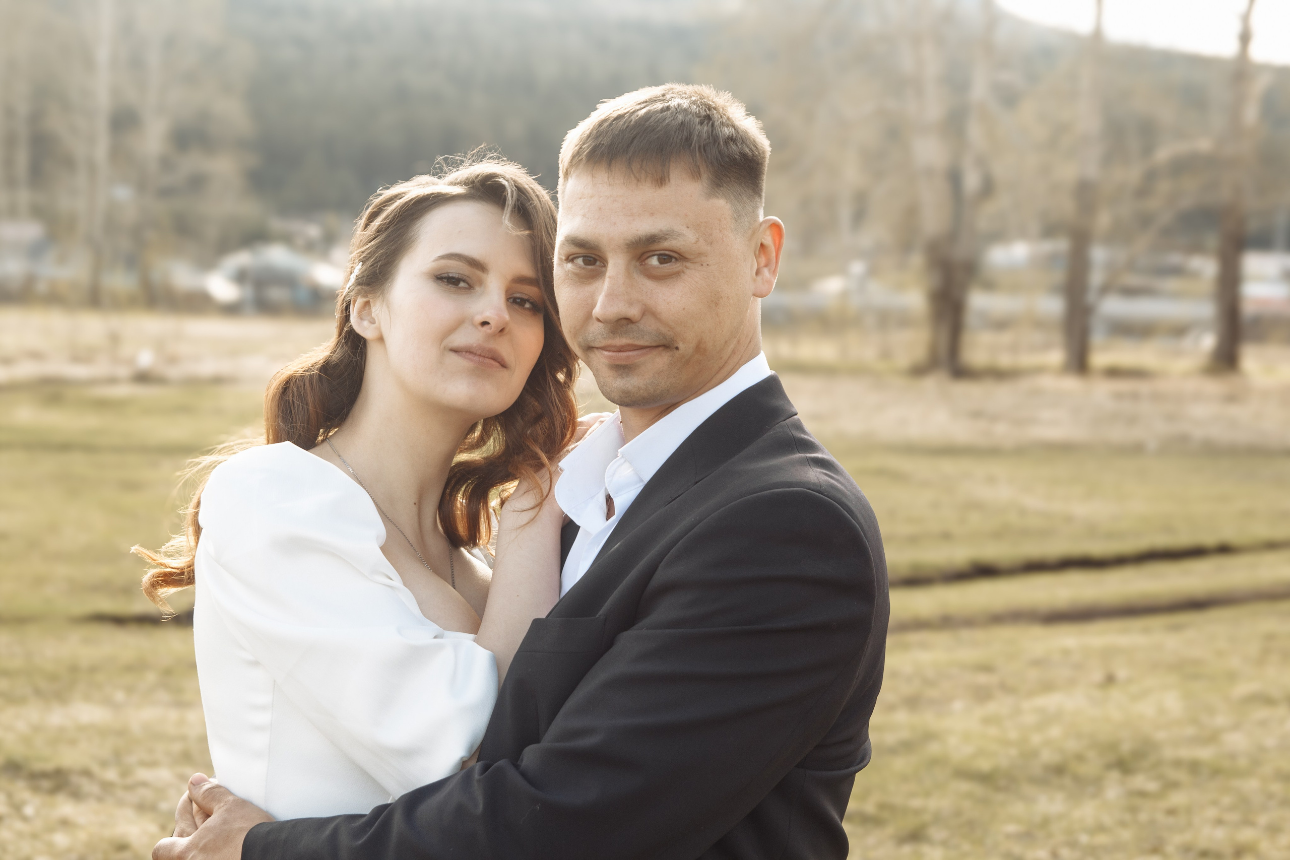 Жених обнимает невесту во время свадебной прогулки, поле и мягкий свет.