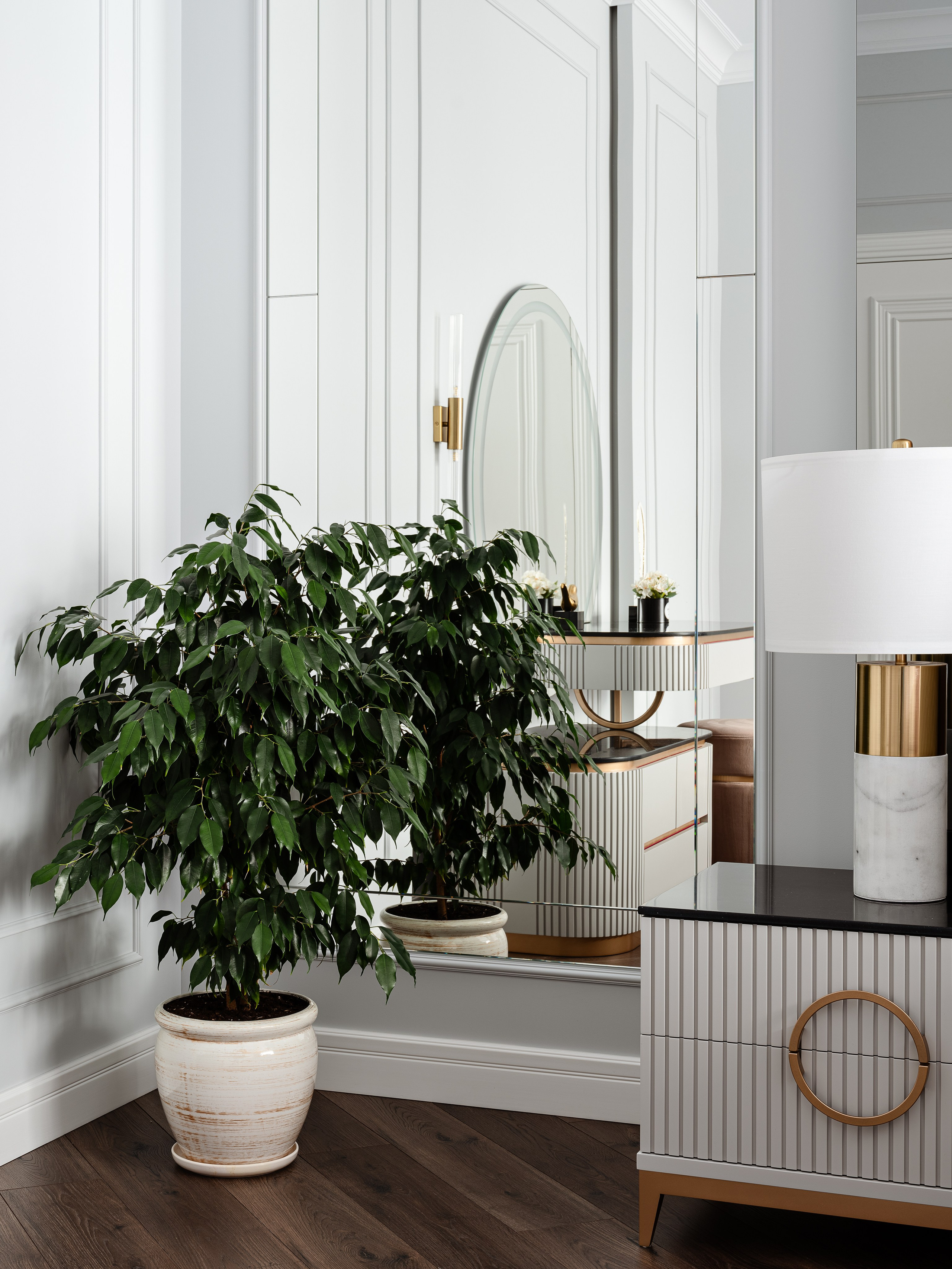 Интерьер спальни с крупным зелёным растением в кашпо, зеркальной стеной и комодом с лампой в мраморном и золотом стиле, гармоничный современный дизайн от Евгении Ермошиной, фото Сергея Денисенко.