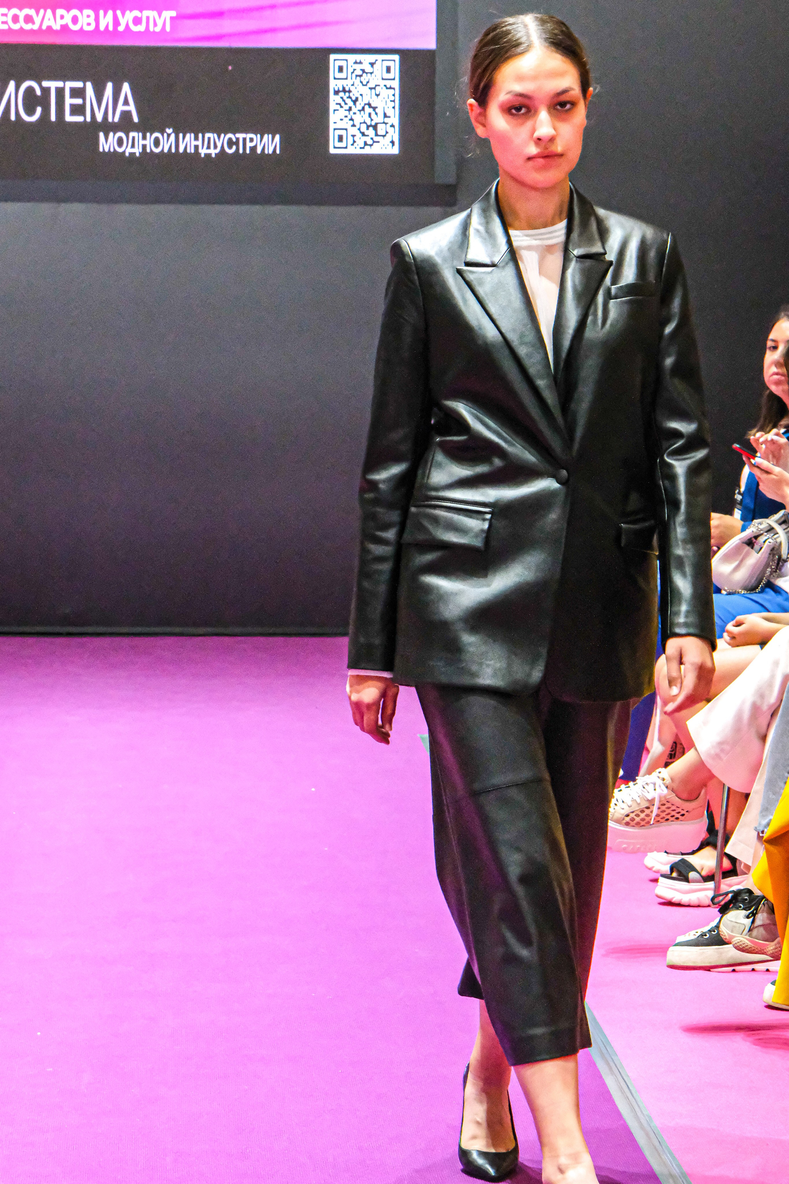  "Модели в ярких нарядах проходят по подиуму во время показа мод, освещенные яркими софитами и окруженные восторженными зрителями."