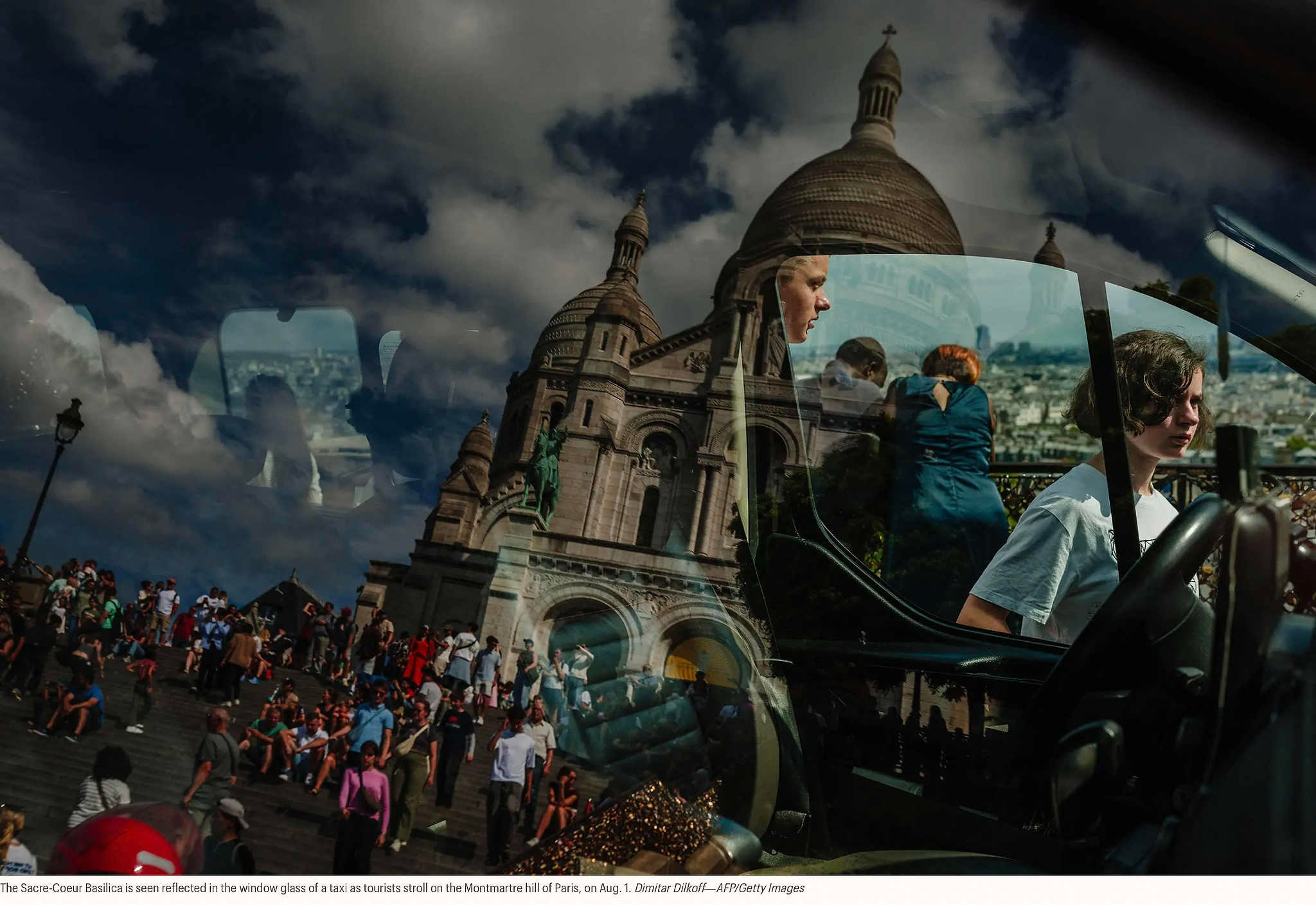 Базилика Сакре-Кер отражается в оконном стекле такси, когда туристы прогуливаются по парижскому холму Монмартр, 1 августа.Димитр Дилкофф —AFP/Getty Images