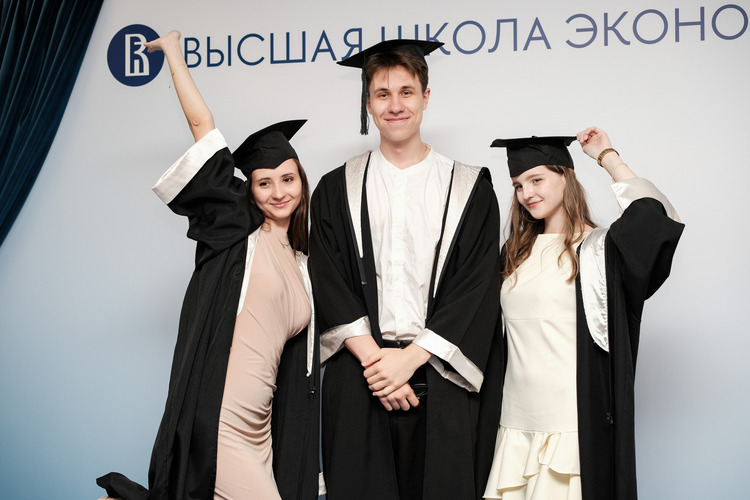 Две выпускницы и выпускник НИУ ВШЭ улыбаются в фотозоне на выпускном