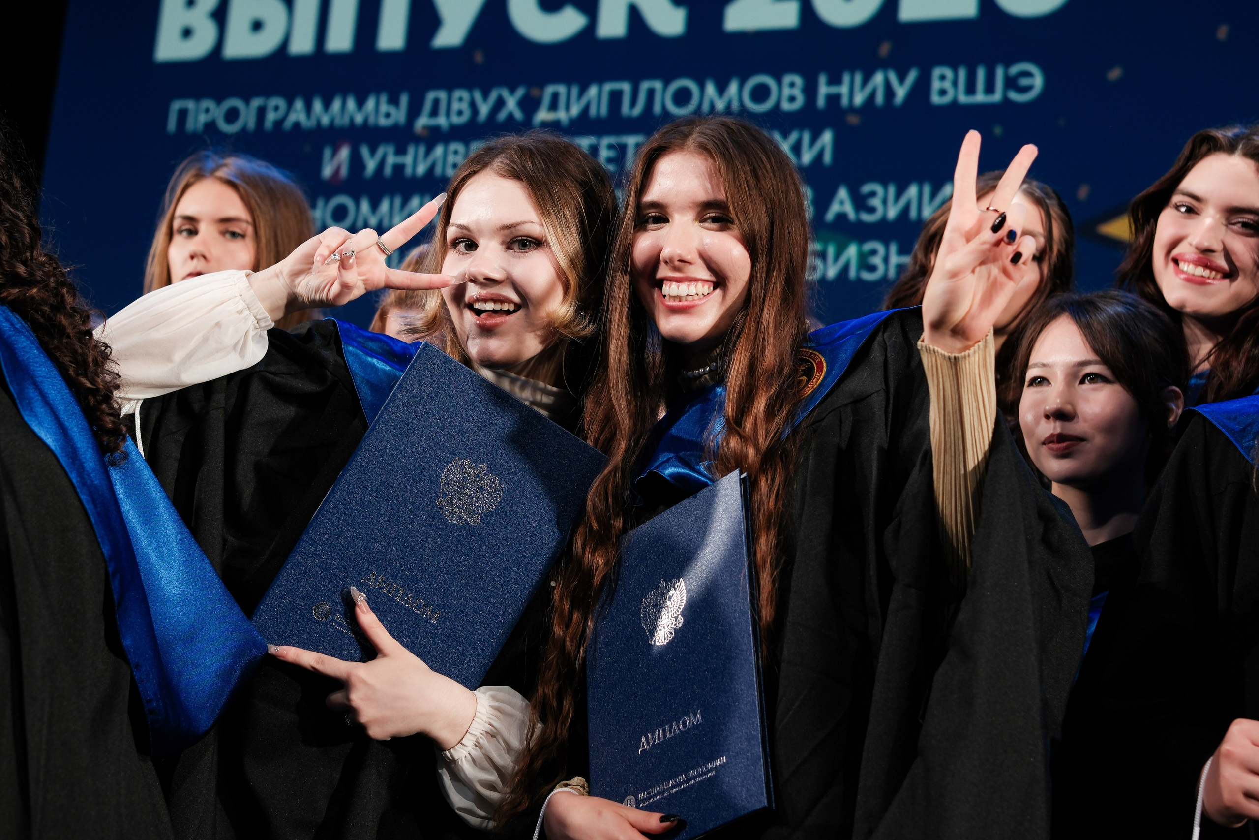 Две выпускницы НИУ ВШЭ показывают знак победы и улыбаются в камеру