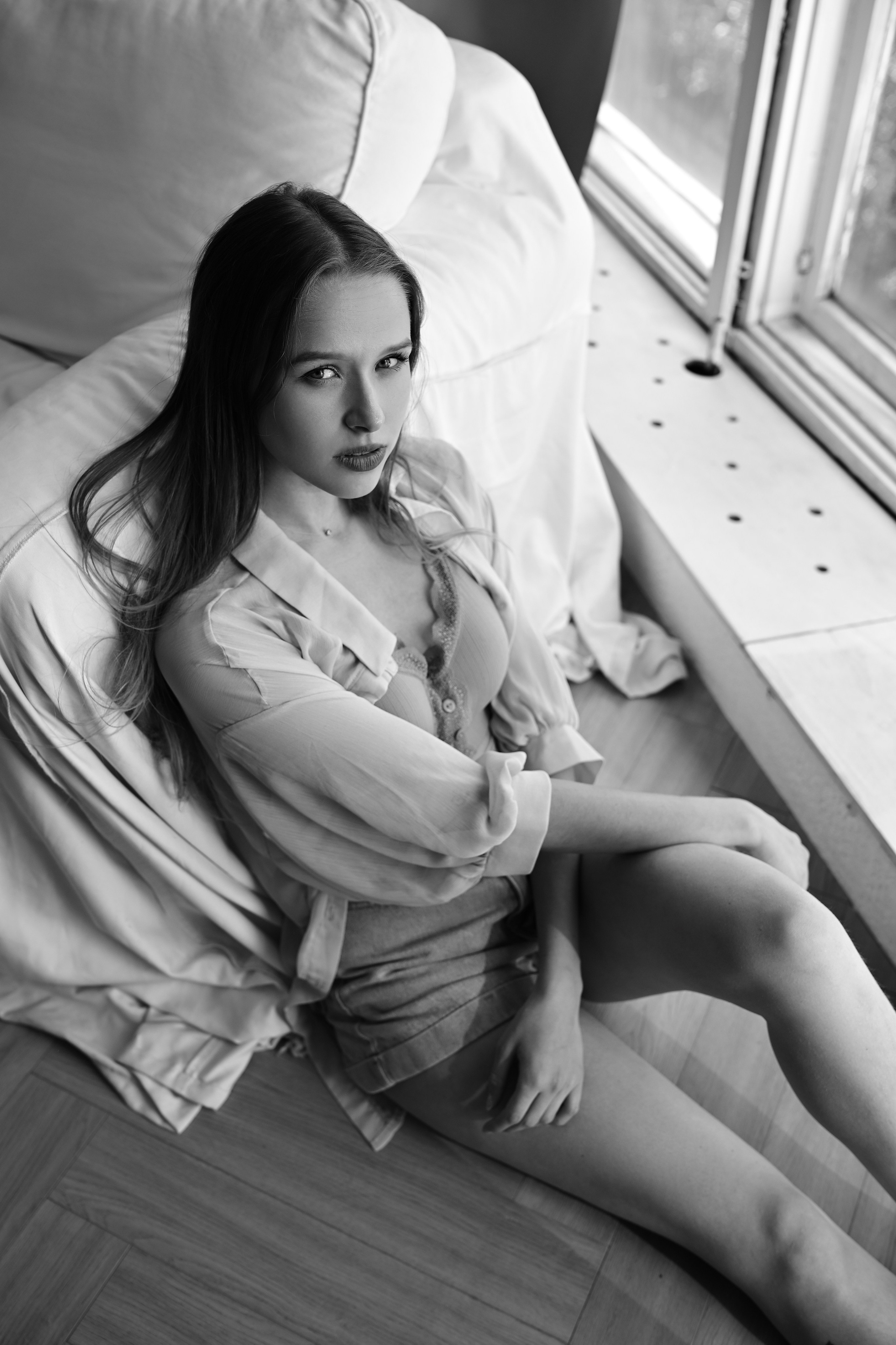 Черно-белая фотография девушки в студийном интерьере с минималистичной атмосферой, мягкими тенями и естественной позой