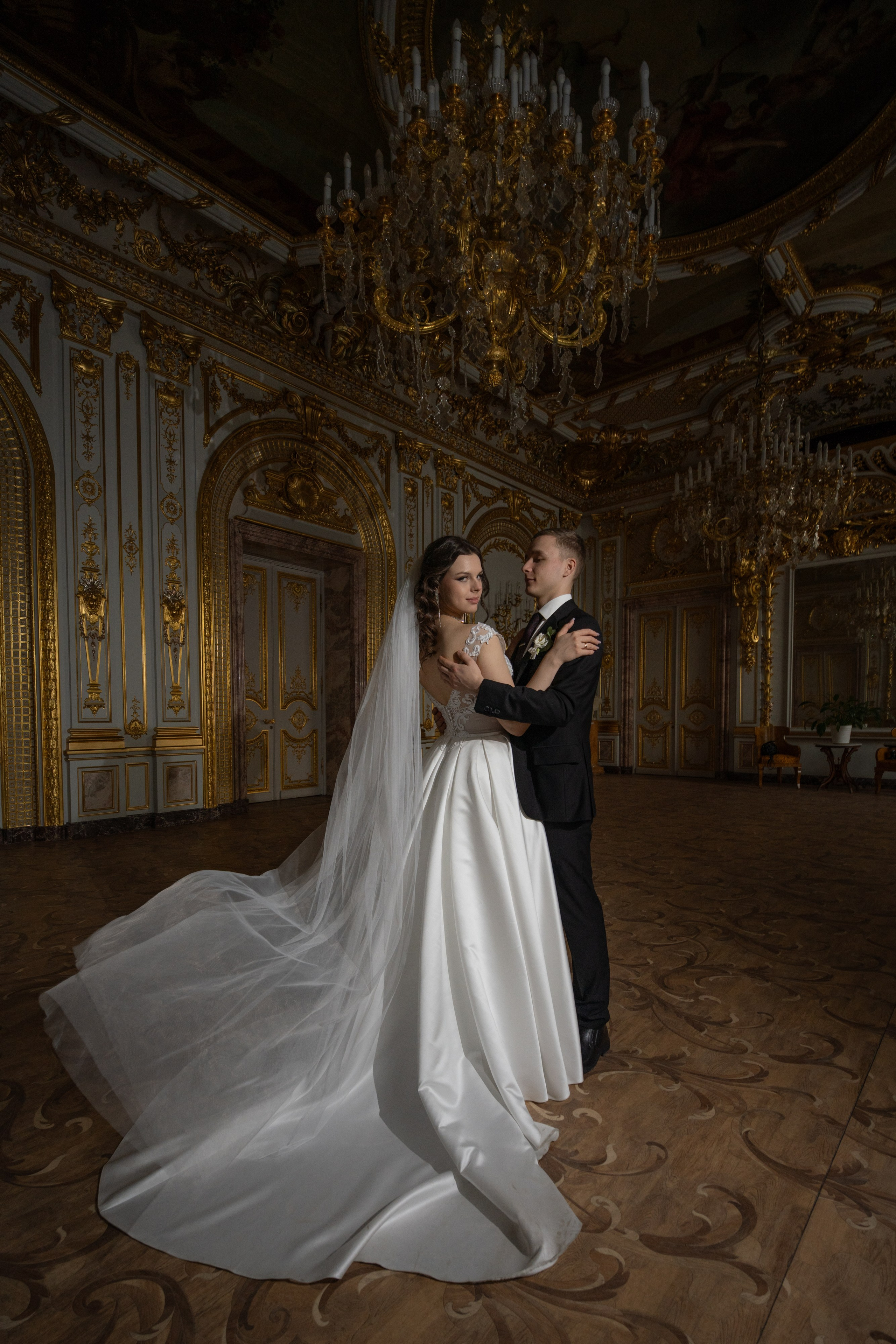 Свадебная фотосессия в Санкт-Петербурге в Особняке Половцева или Дом Архитектора. Свадебная пара красиво стоит в золотом зале с красивыми люстрами