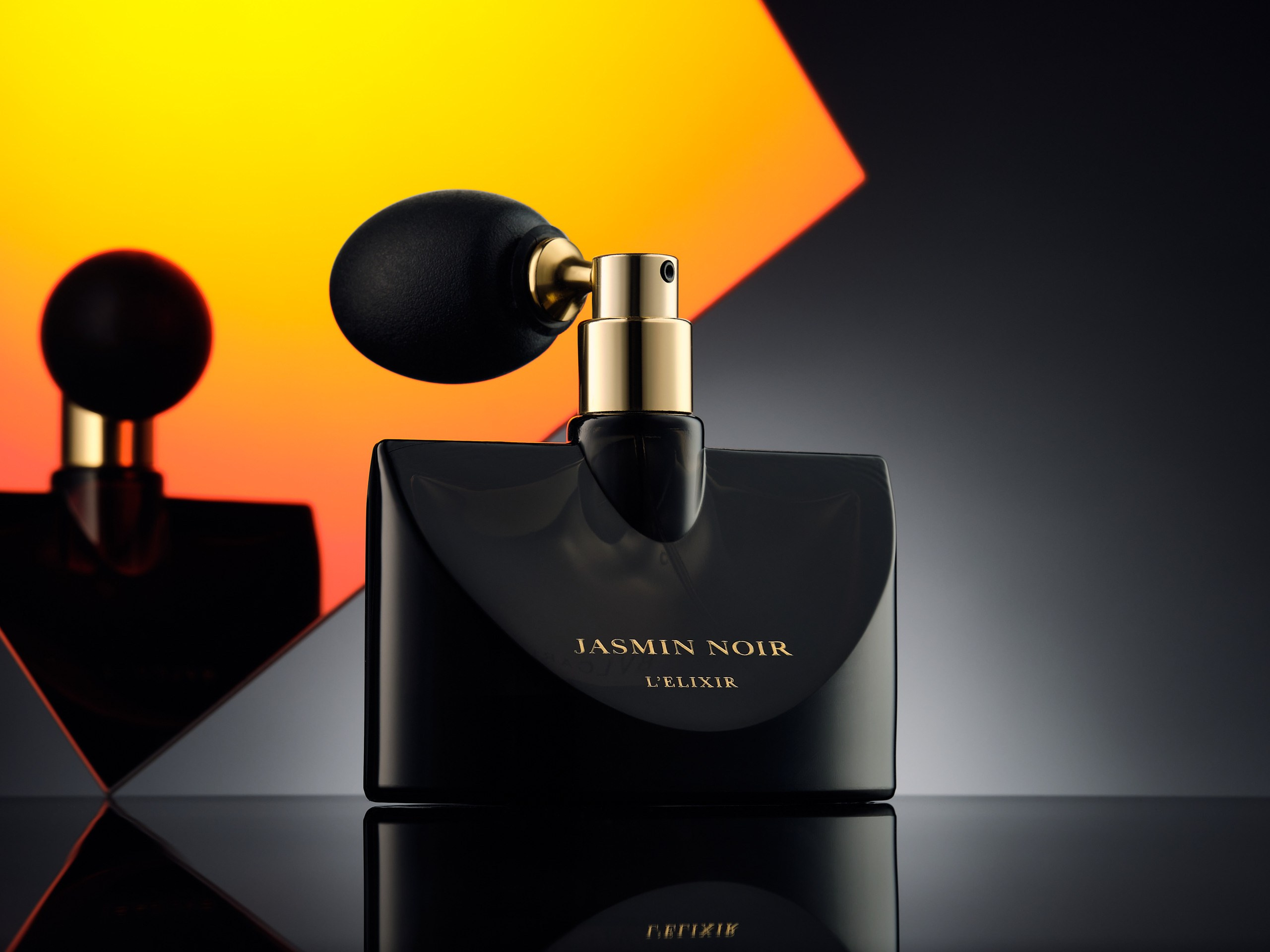 Черный флакон духов с ретро-пульверизатором на фоне апельсиновой подсветки