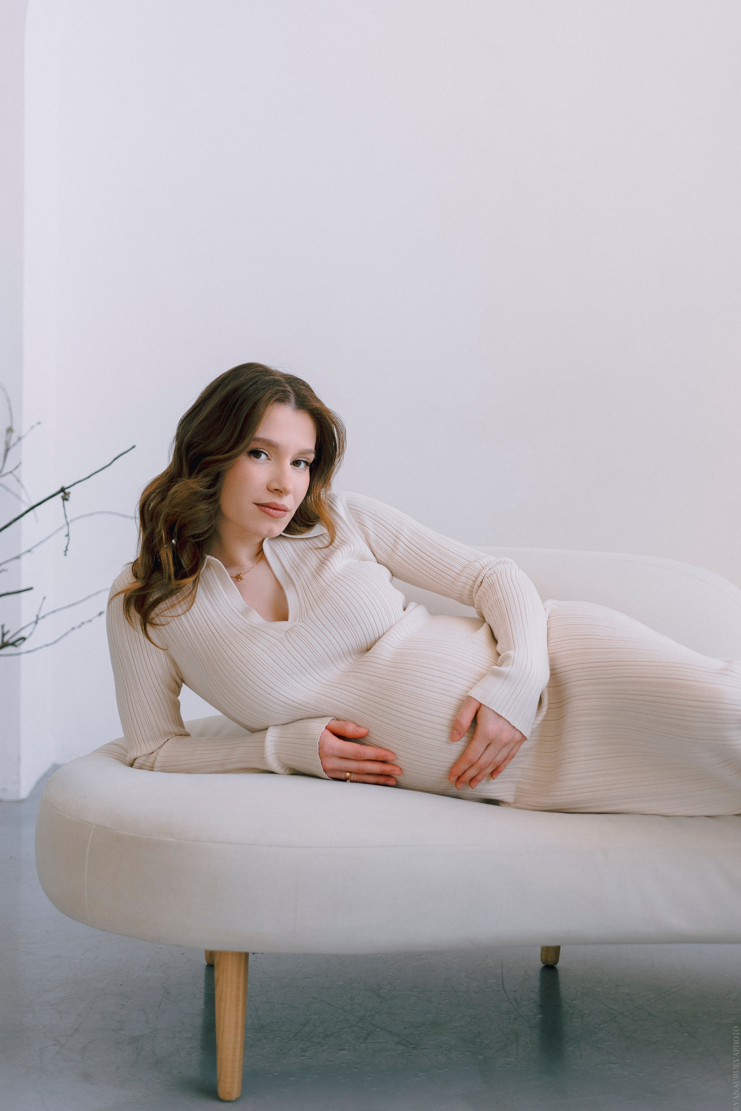беременная девушка в светлом платье и с локанами на диване
