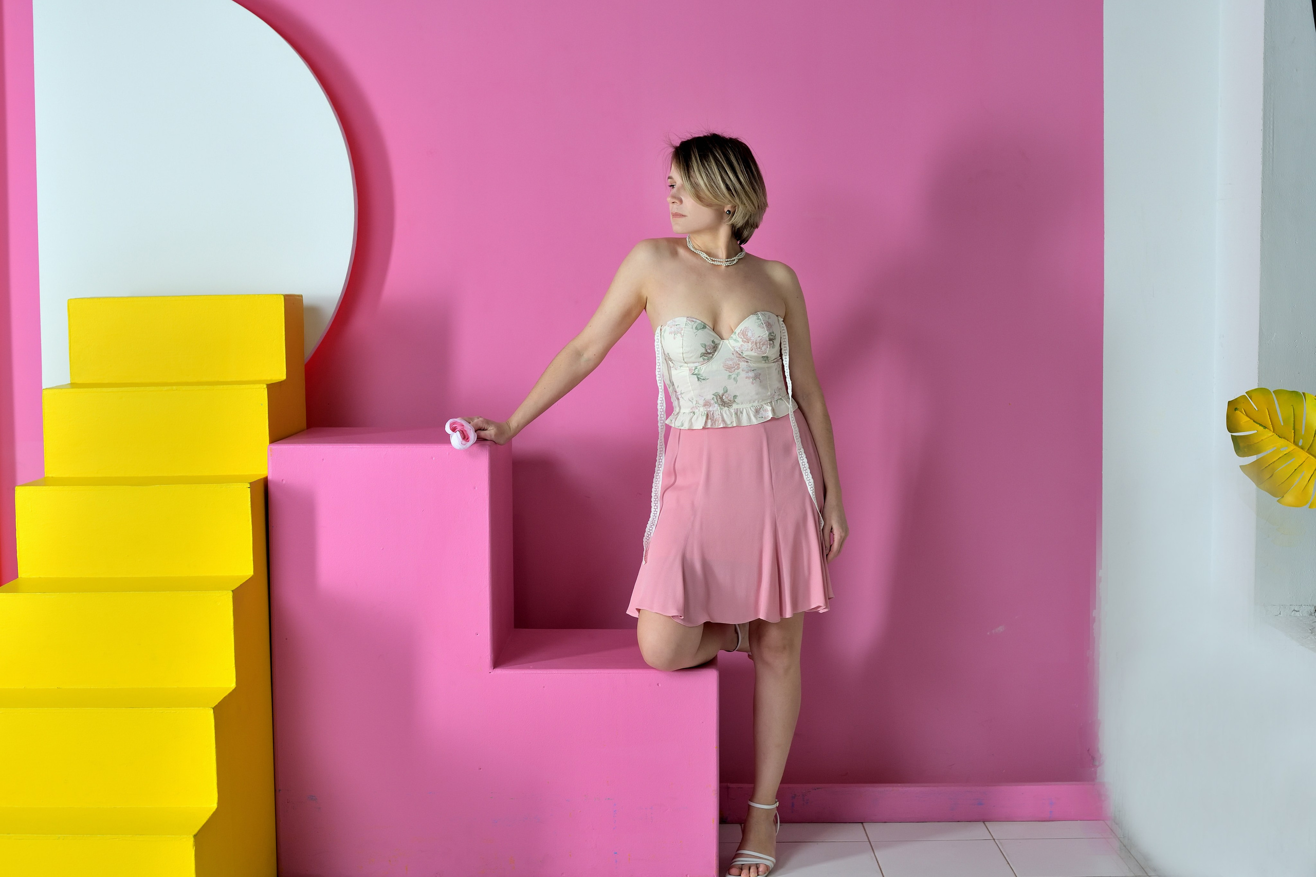 Девушка в розовой юбке позирует на фоне розовый стены в фотостудии.