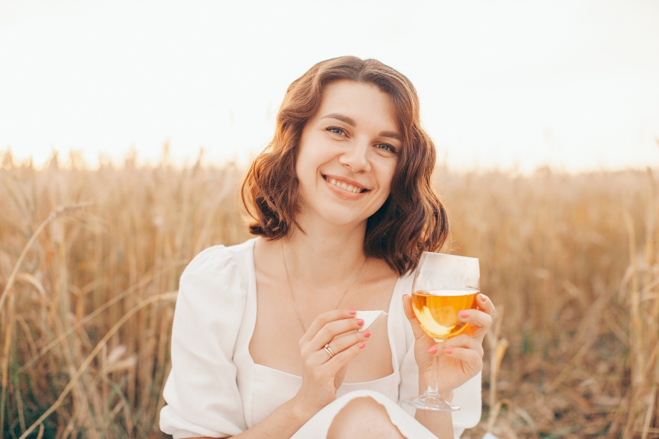 Девушка в поле с бокалом вина улыбается