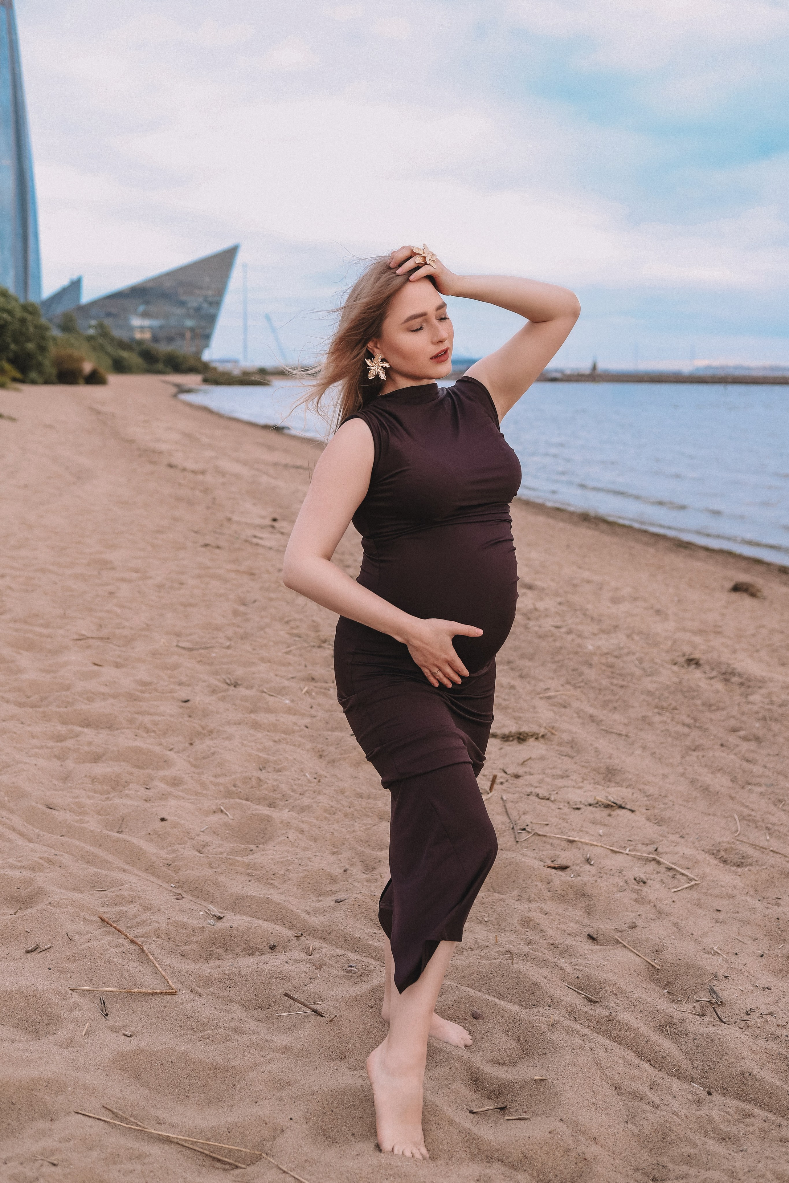 Беременная девушка в чёрном платье идёт по пляжу, фотосессия у воды