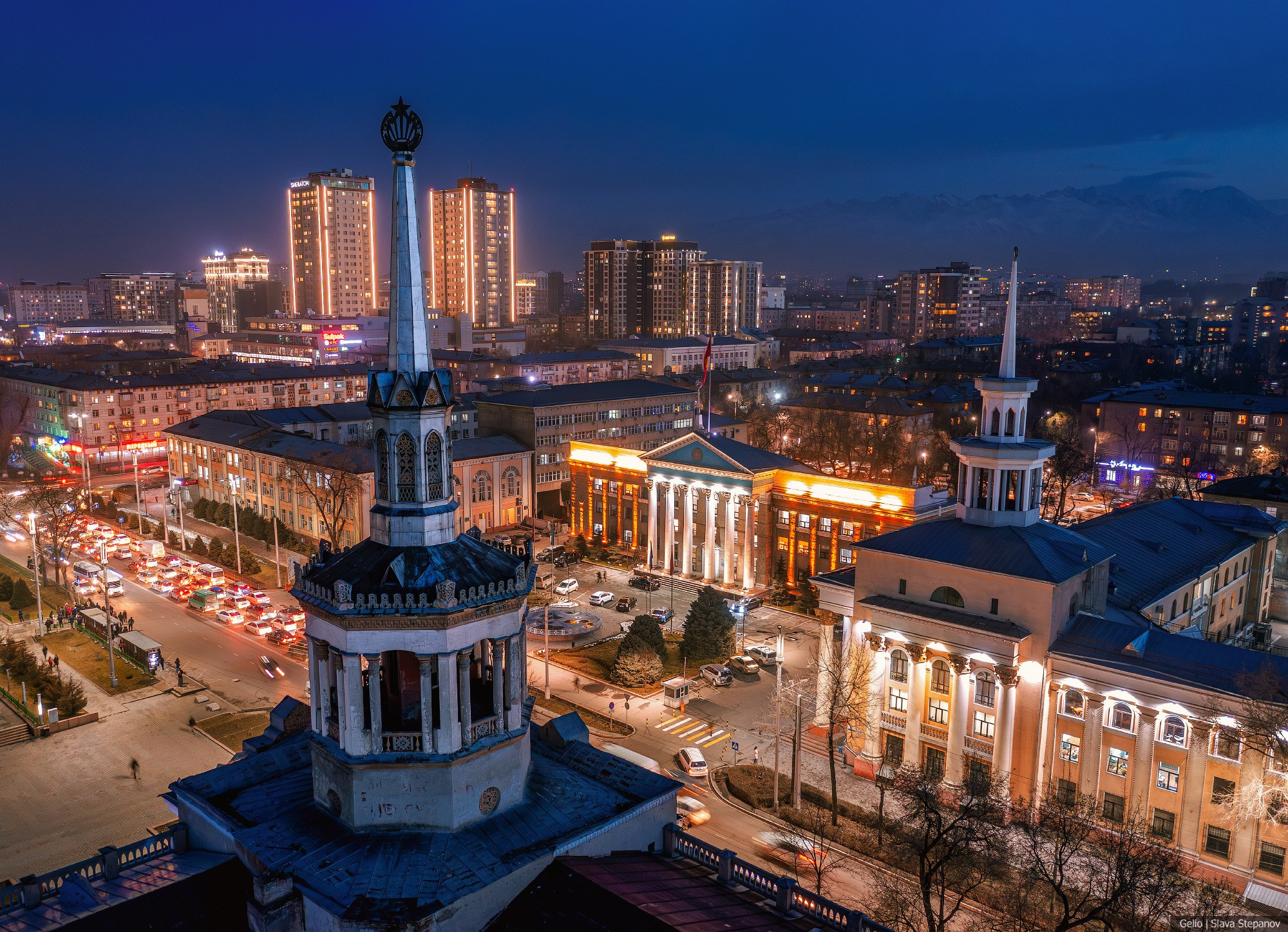 Ночной вид с высоты на центральную часть Бишкека в Кыргызстане. На переднем плане — исторические здания со шпилями, на заднем плане — современные высотные комплексы и силуэты гор. Фотограф: Слава Степанов.