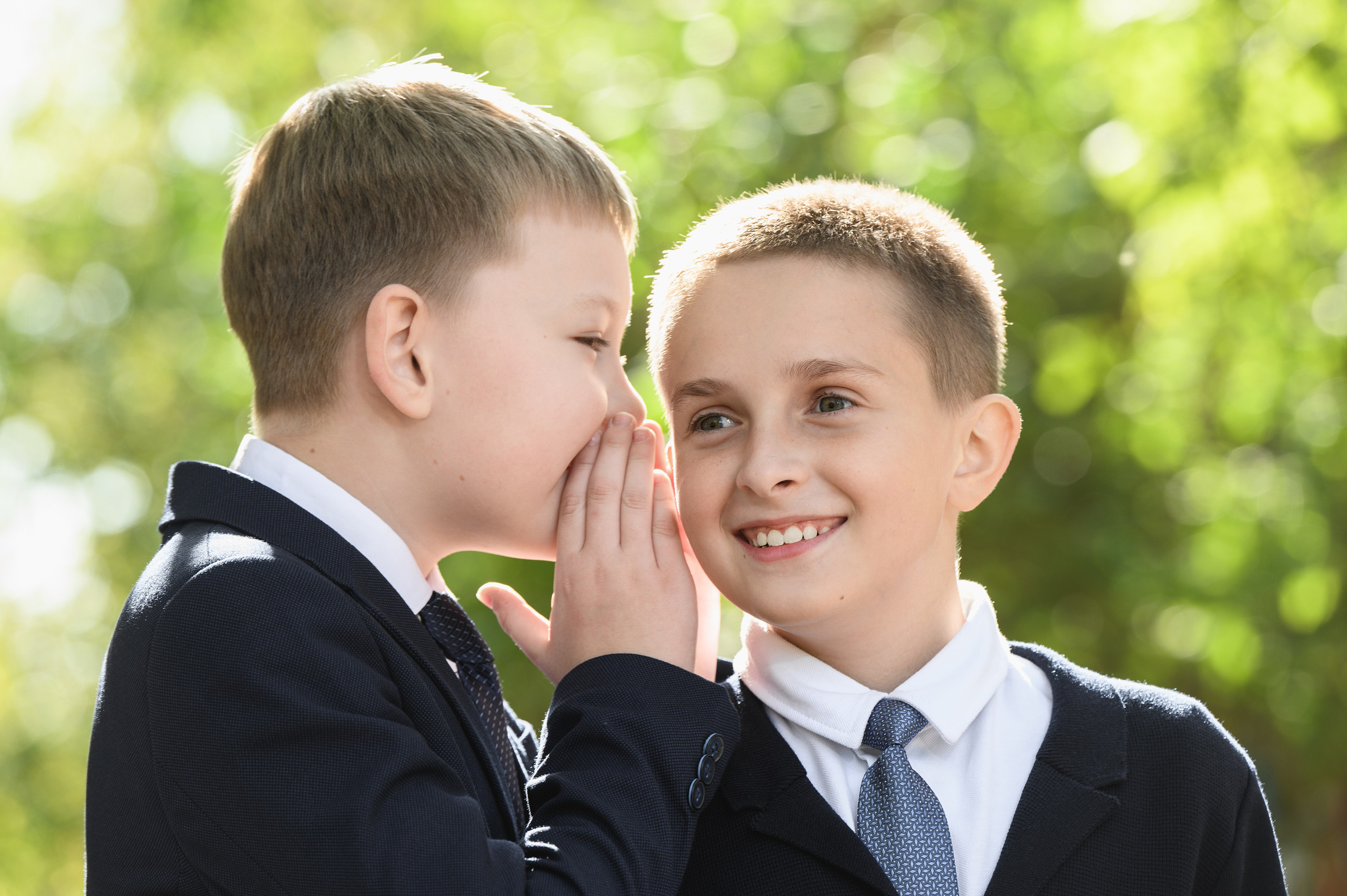 Мальчик шепчет однокласснику на школьном дворе